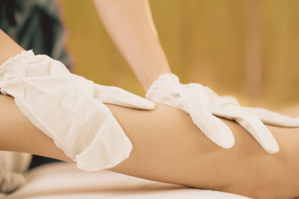 Person receiving a massage on their arm, wearing white gloves, in a spa or wellness setting.