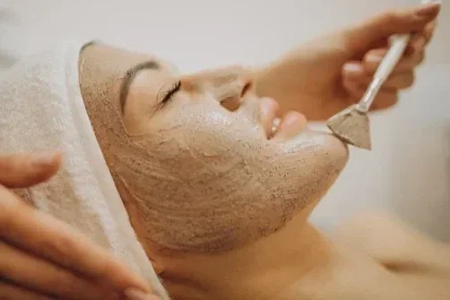 A woman receiving a facial treatment with a facial mask applied, lying down with her eyes closed.