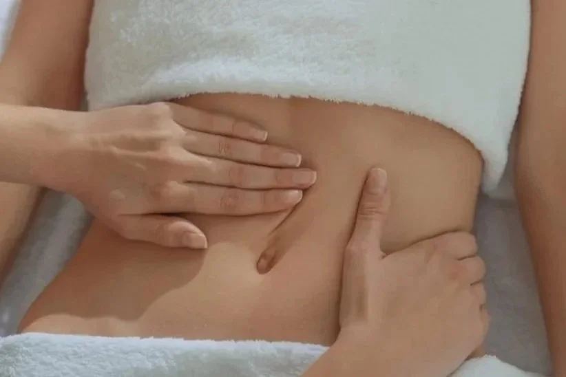 Close-up of a person receiving a massage on their stomach, with hands pressing on their bare abdomen, lying on a white towel.