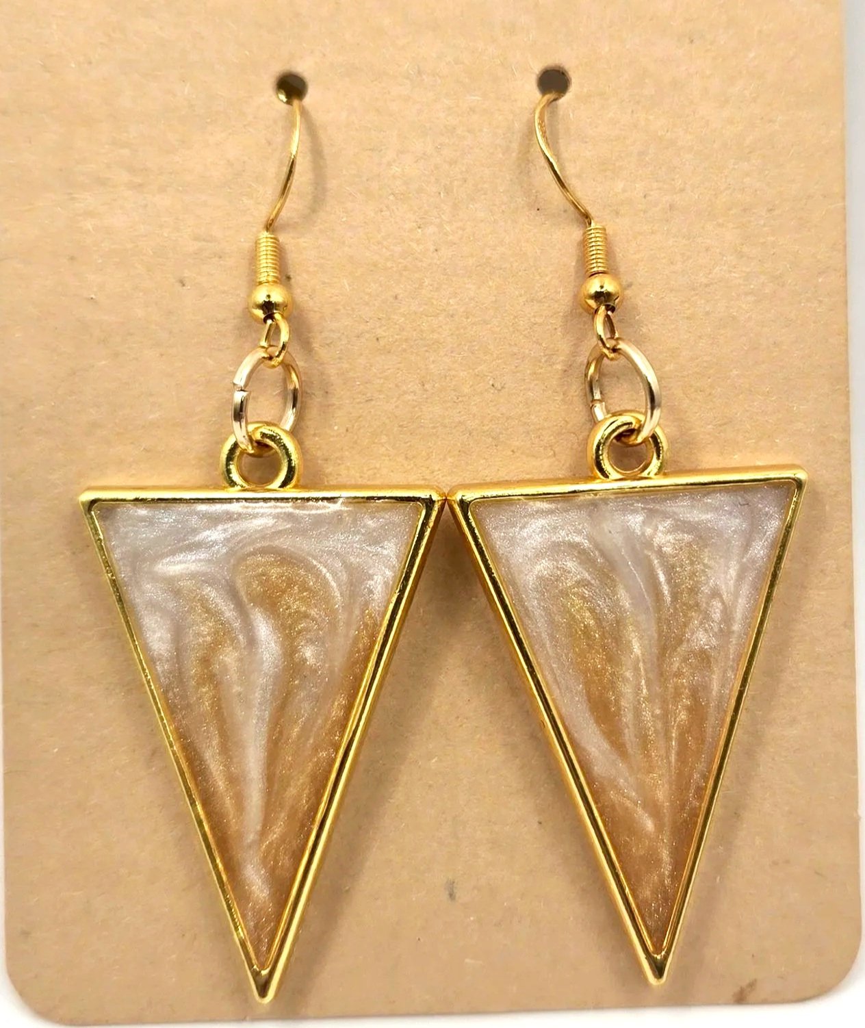 Gold-colored triangle-shaped resin earrings with swirling beige and white patterns, hanging from fishhook style wires.