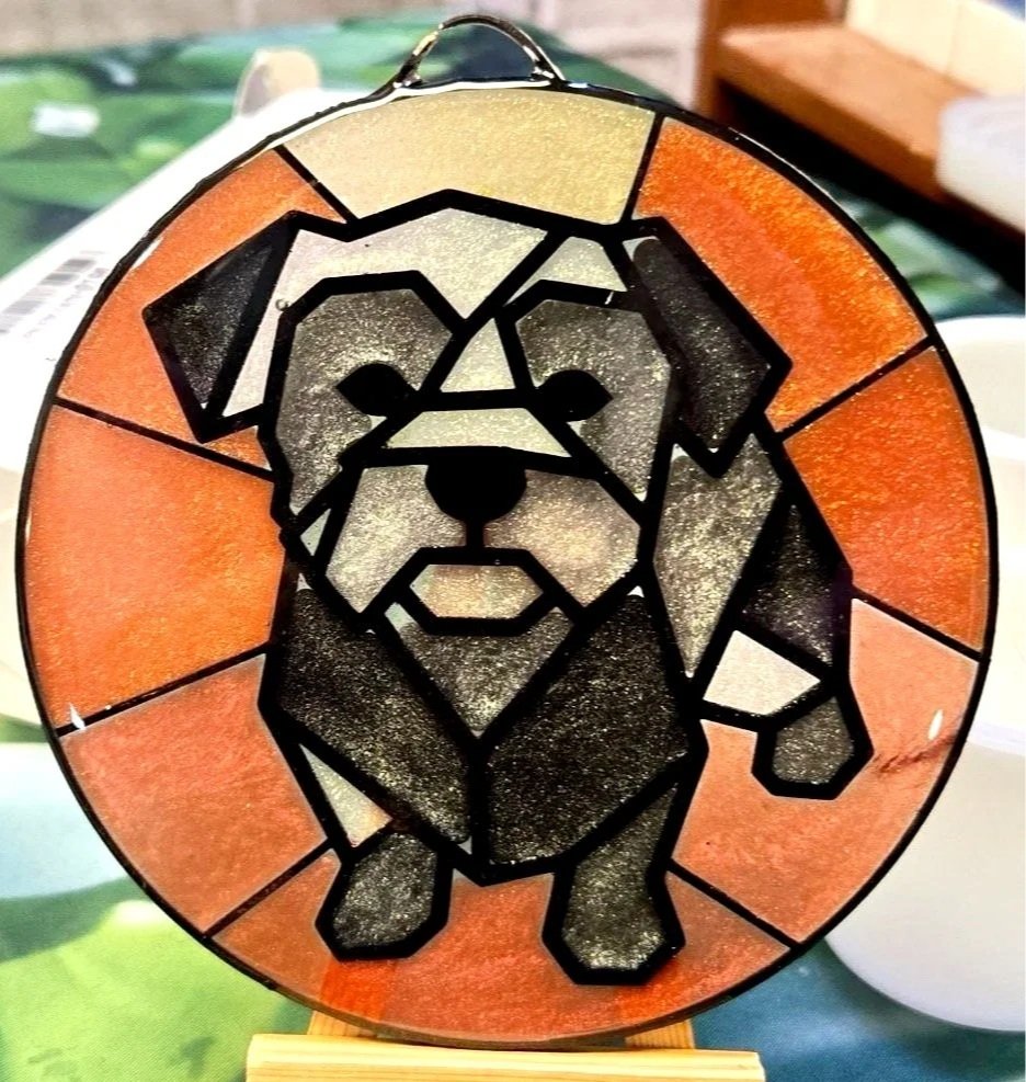 Stained glass art depicting a dog, with black outlined geometric shapes filled with shades of black, white, and orange.