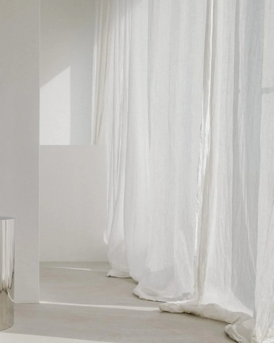 White curtains hanging in a minimalist, light-colored room with a floor and walls in shades of white and beige.