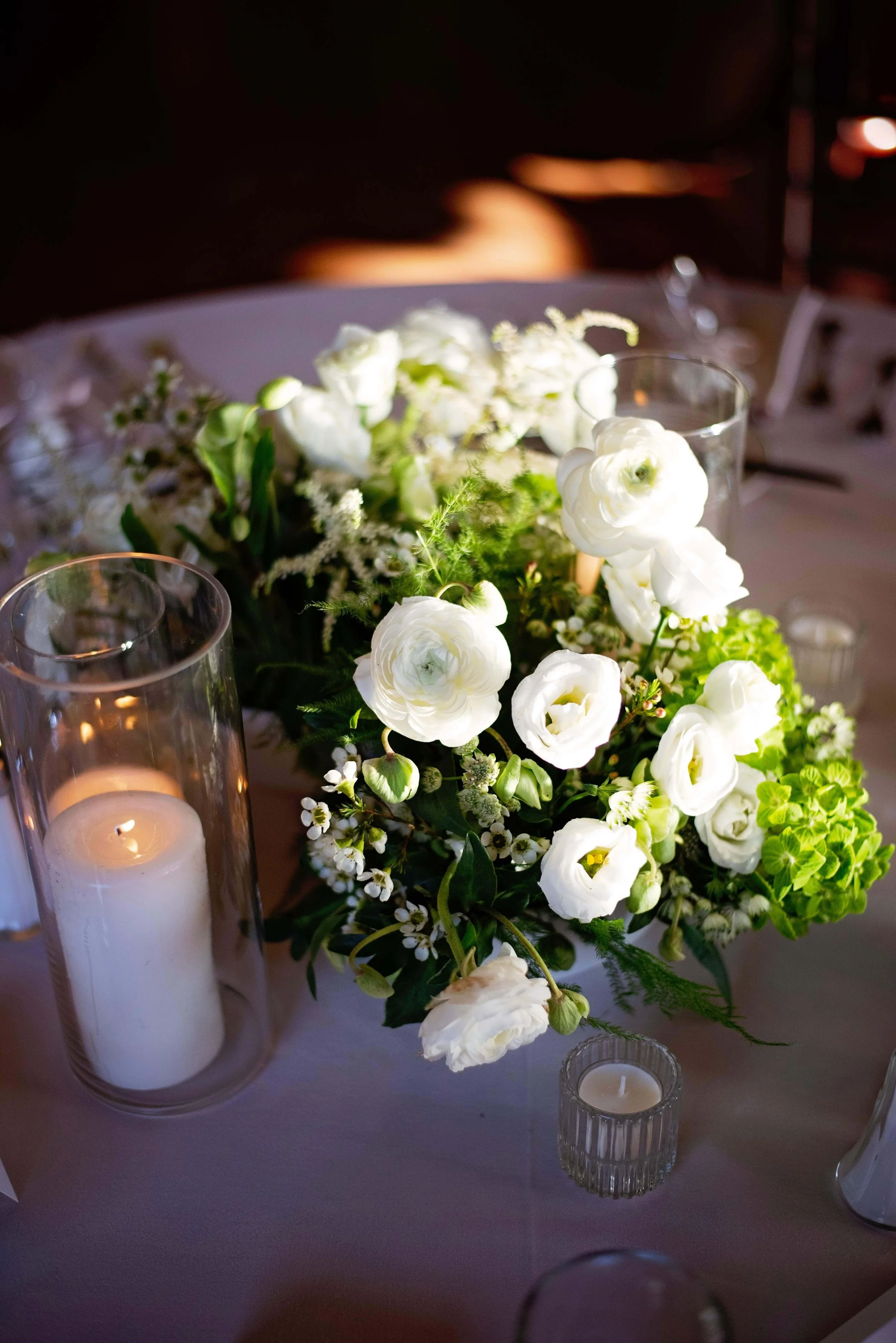 Low centerpiece of white ranunculus, green hydrangea, waxflower, and astilbe with pillar candle at Newfound Lake Inn, Bridgewater New Hampshire wedding florals by Milkweed Floral Co