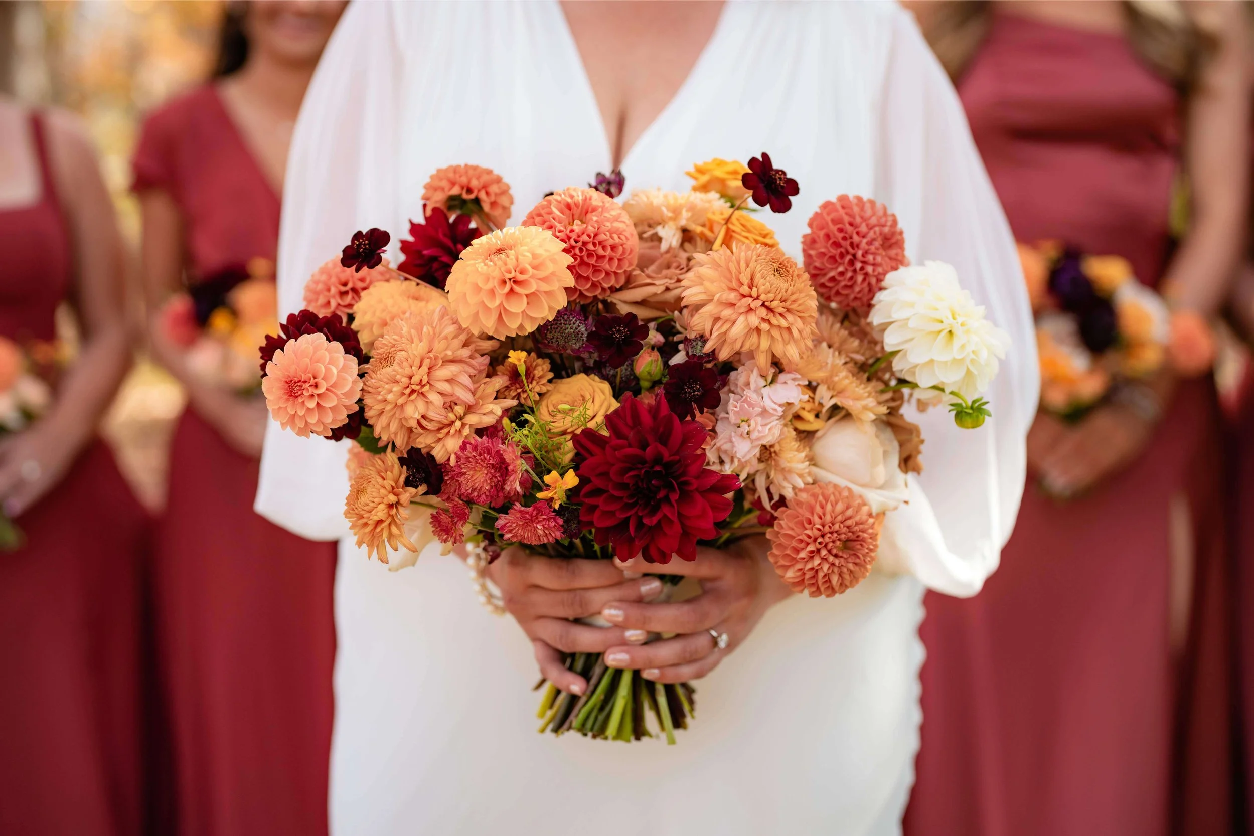 Colorful fall bridal bouquet with peachy, yellow, orange dahlia pompons held by a bride, autumn Maine wedding by Milkweed Floral Co