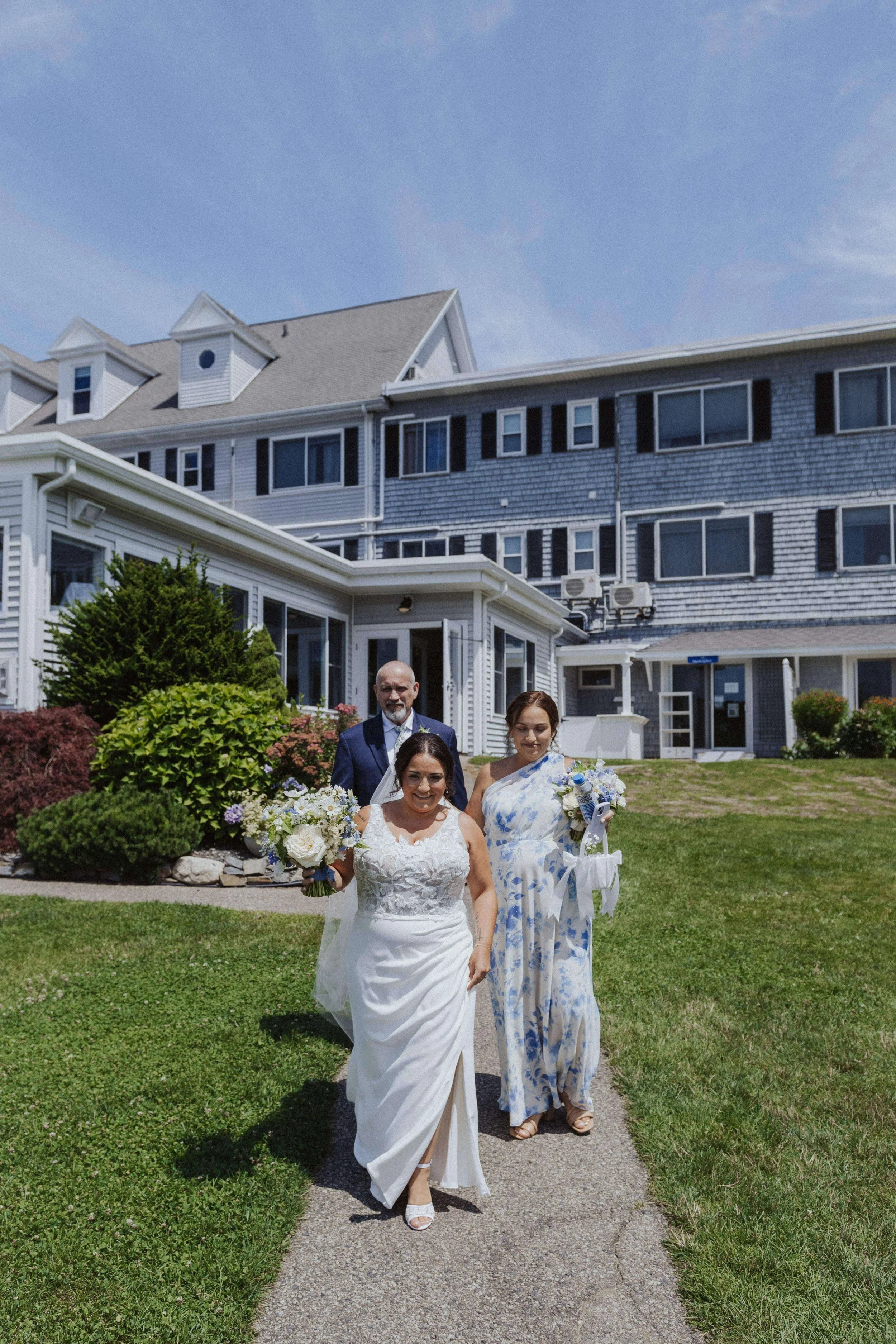 Bride holding lush white bouquet, walking next to parents at The Nonantum Resort, florals by Milkweed Floral Co