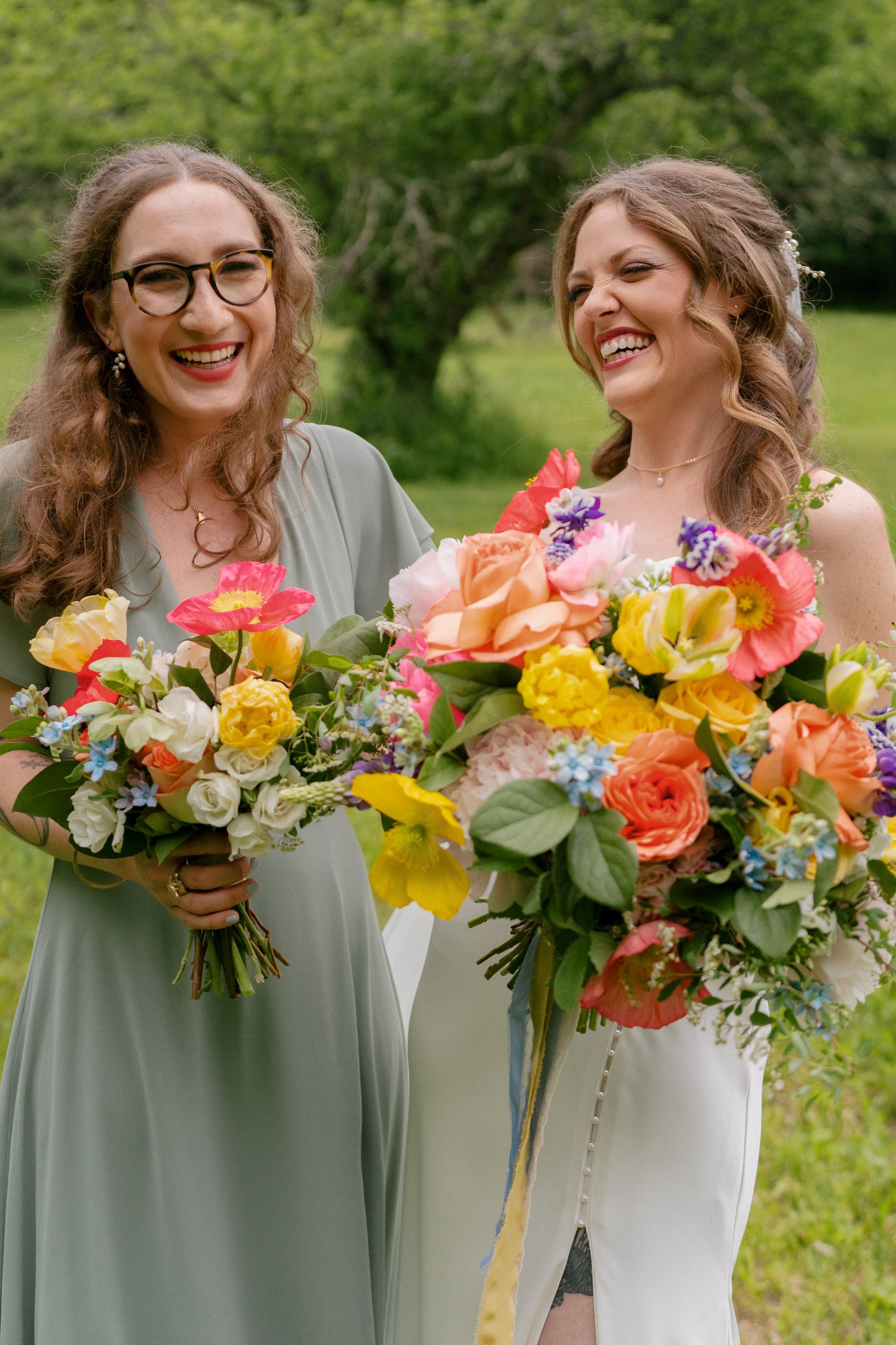 Laughing bride and bridesmaid in sage green dress holding vibrant spring bouquets of poppies, garden roses, yellow tulips, and blue forget-me-nots, Montague Massachusetts wedding by Milkweed Floral Co