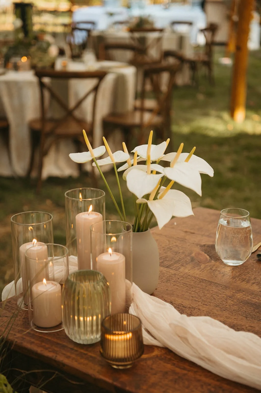 Modern minimalist wedding centerpiece with white anthurium in a matte ceramic vase surrounded by pillar candles in glass hurricanes on a wood farm table, Monson Massachusetts, Milkweed Floral Co