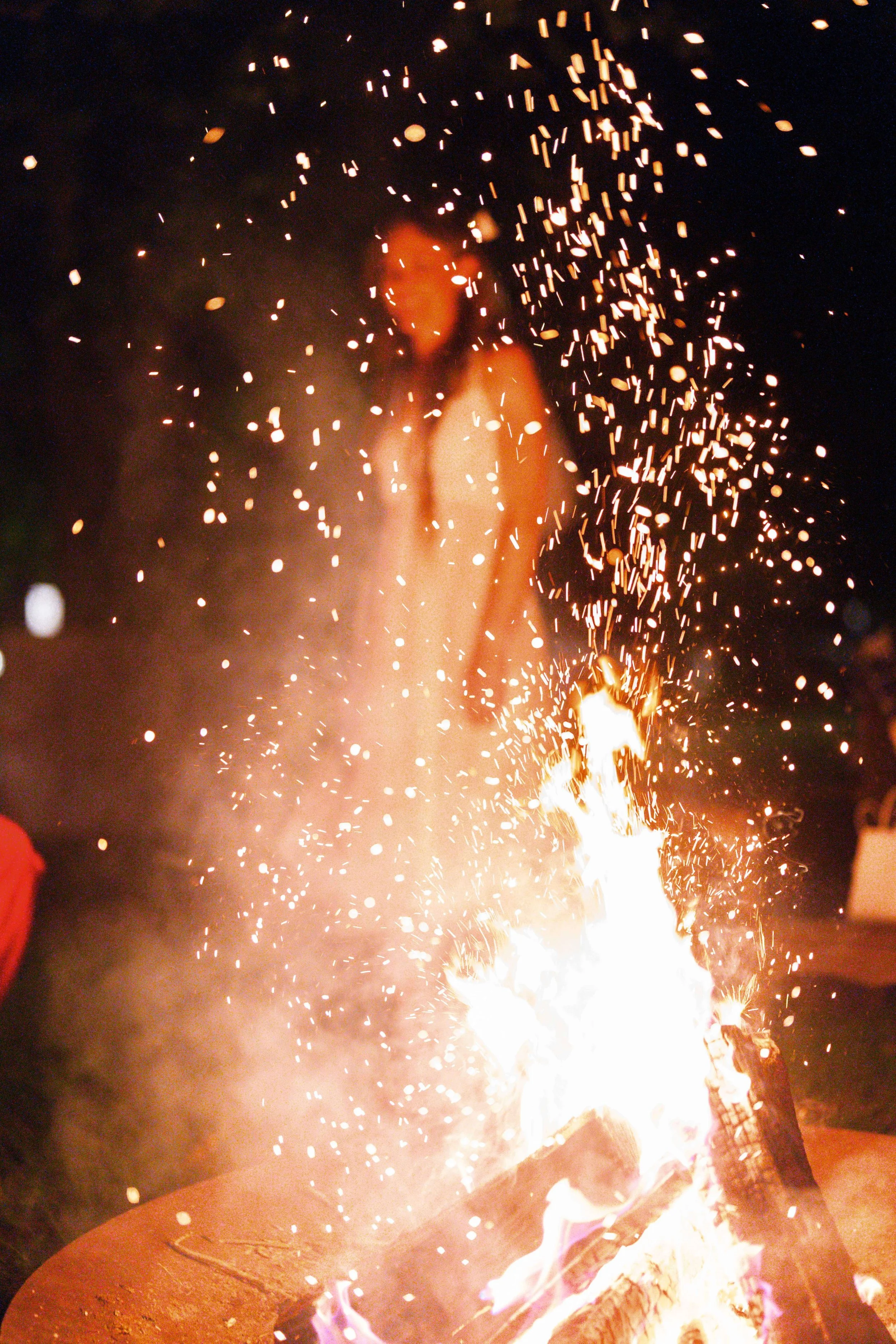 Bride silhouetted behind a crackling bonfire with sparks flying at a nighttime outdoor wedding reception, Montague Massachusetts, Milkweed Floral Co
