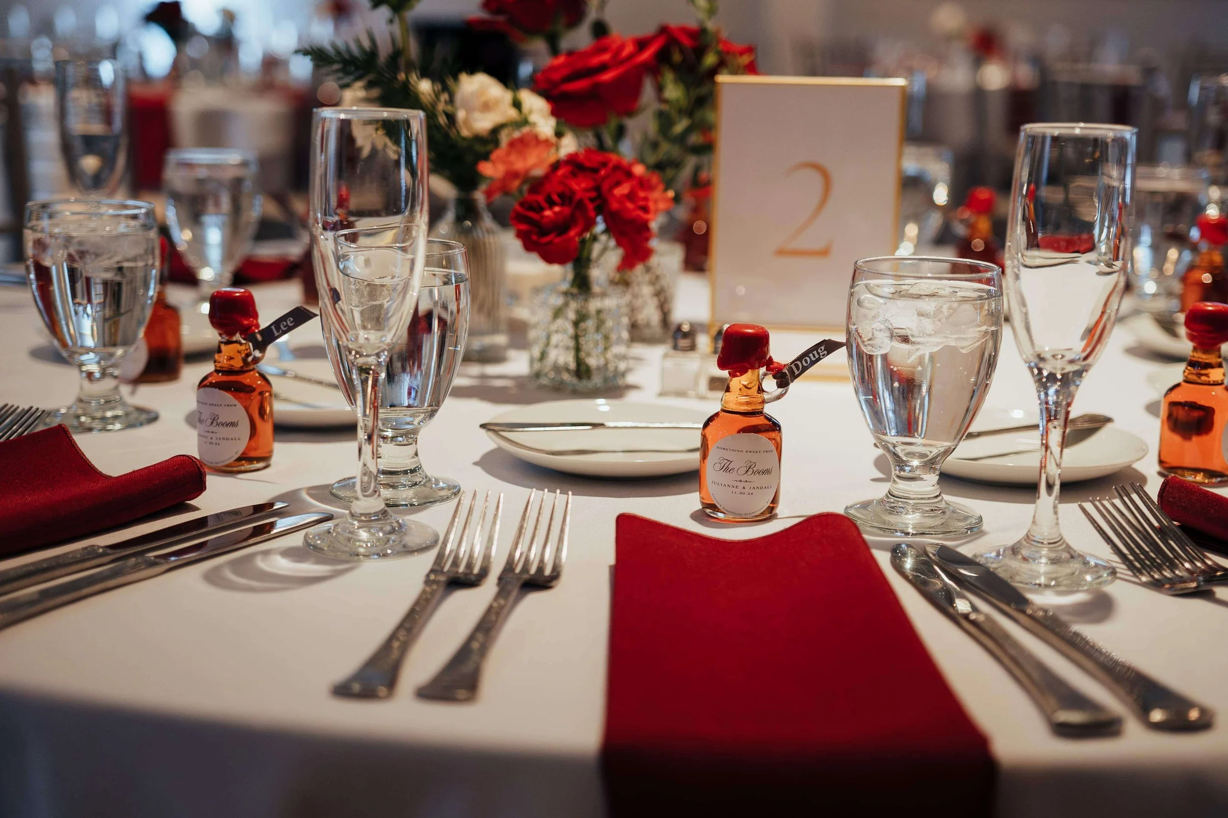 Classic reception table setting with red rose centerpiece, red napkins, and personalized mini bourbon favors at Saphire Estate, Sharon Massachusetts wedding florals by Milkweed Floral Co