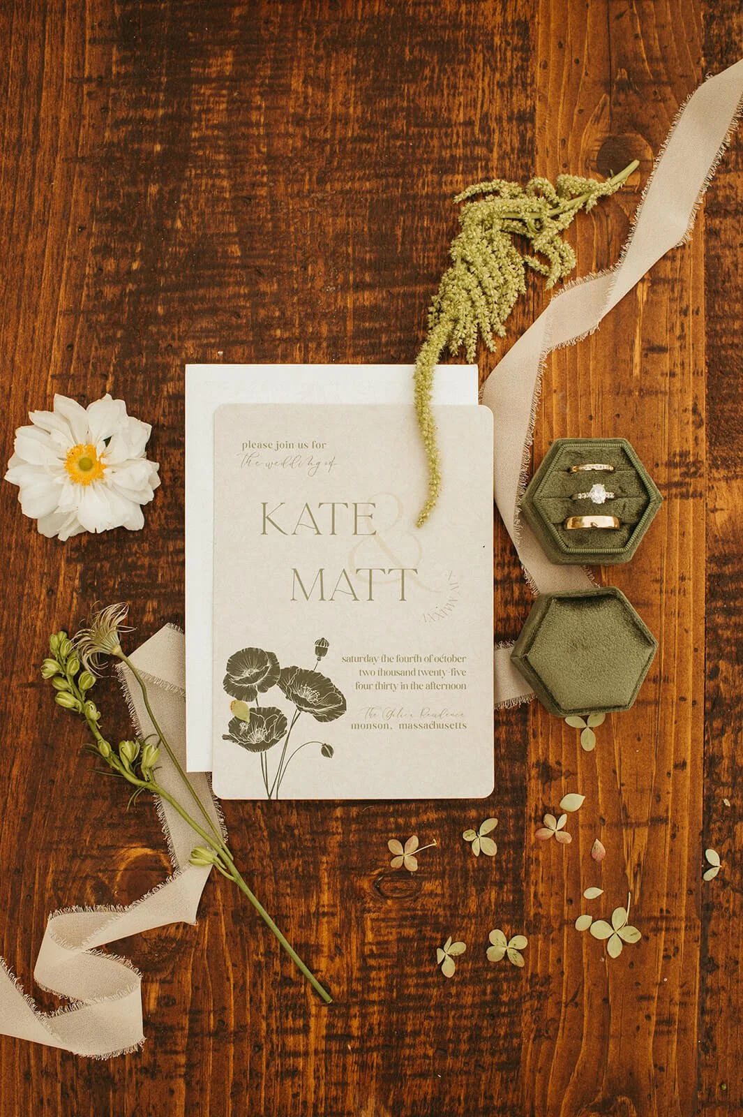 Modern wedding invitation flatlay with botanical poppy illustration, green velvet ring box, white cosmos, and trailing amaranthus on a wood surface, Monson Massachusetts wedding by Milkweed Floral Co