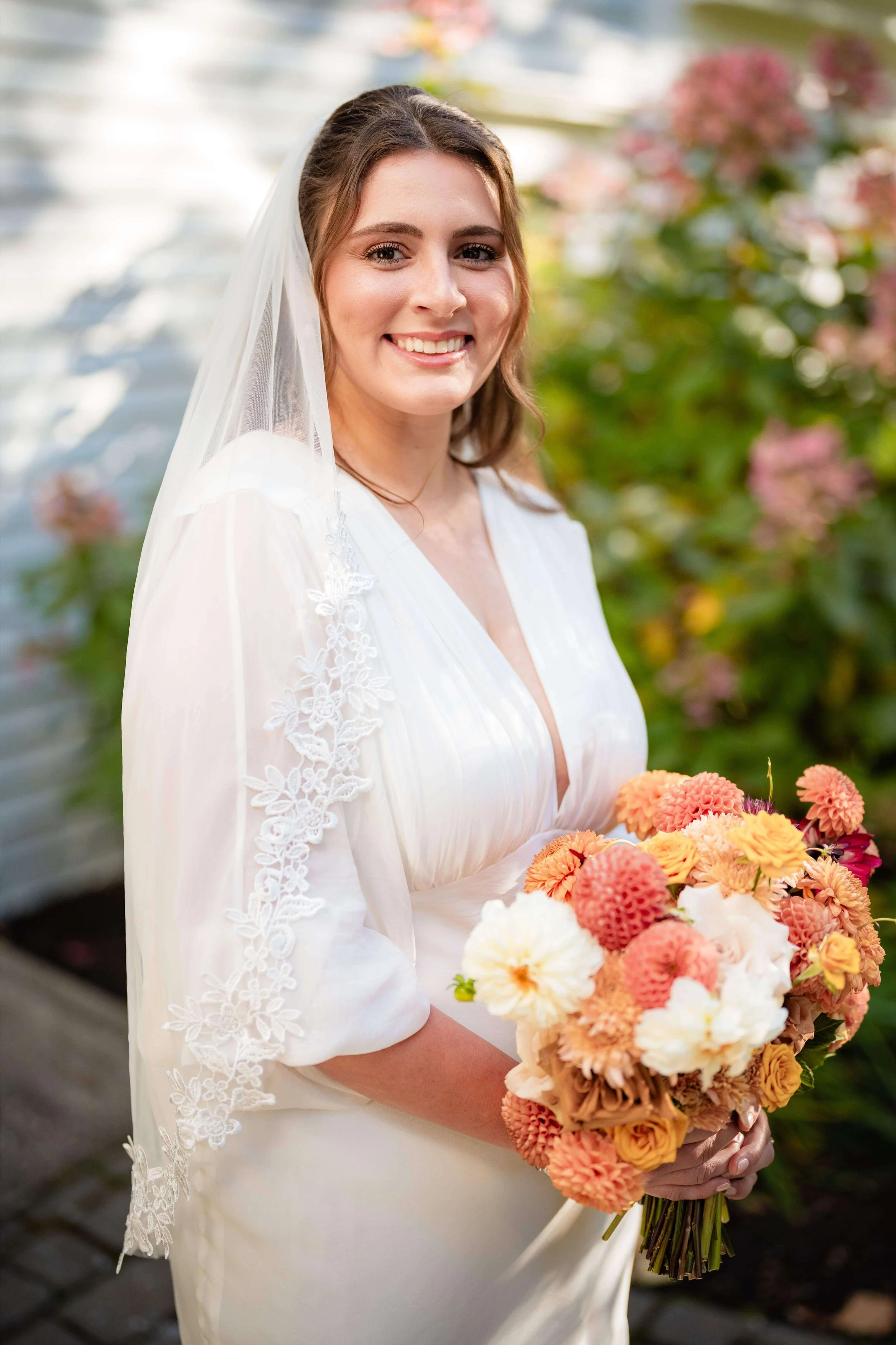 Smiling bride in veil holding blush, yellow, peachy dahlia pompon bouquet,outdoor fall Maine wedding by Milkweed Floral Co