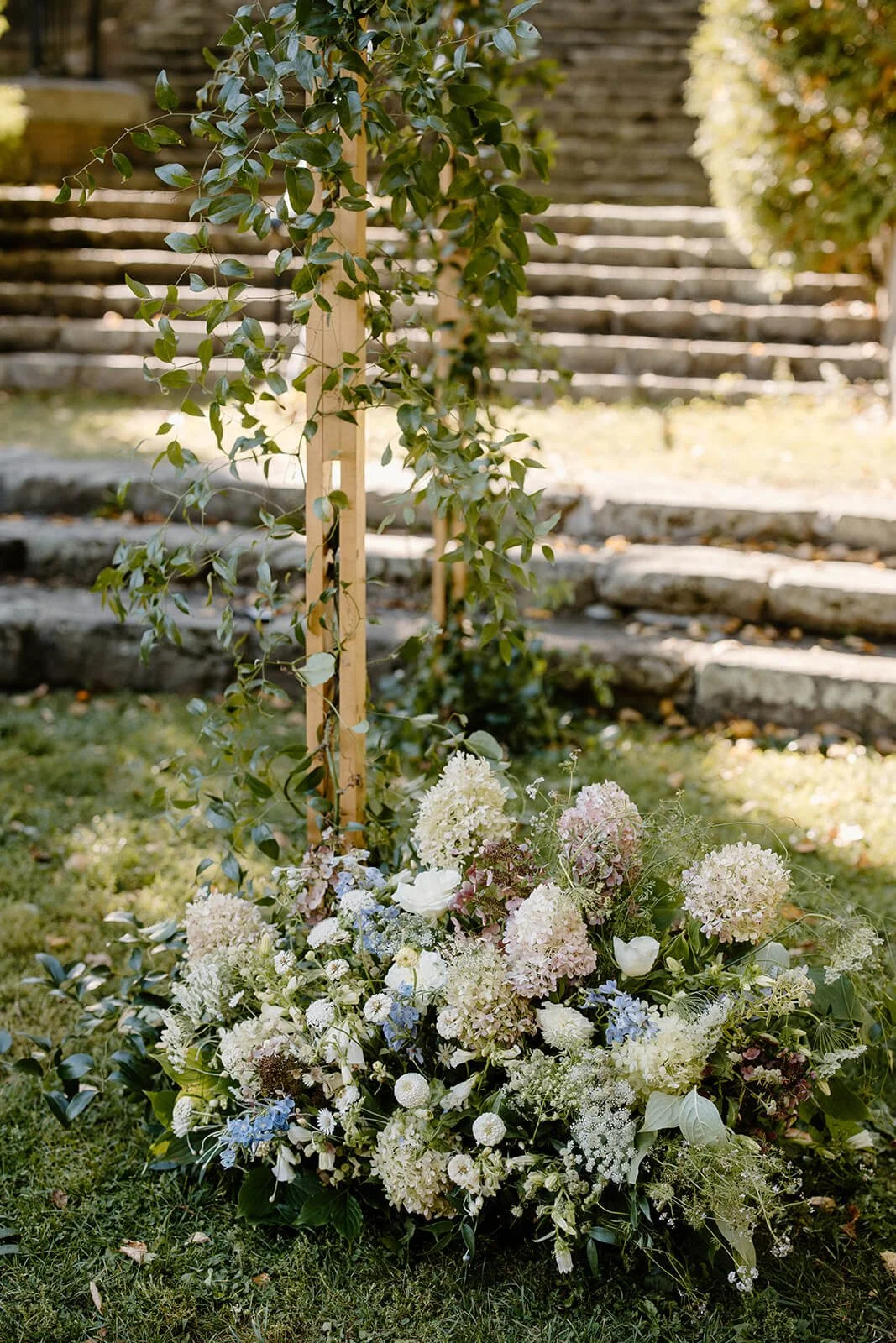 Lush chuppah base arrangement with blush and white hydrangea, blue delphinium, dahlia pompons, and trailing greenery at Camden Public Library, coastal Maine wedding by Milkweed Floral Co
