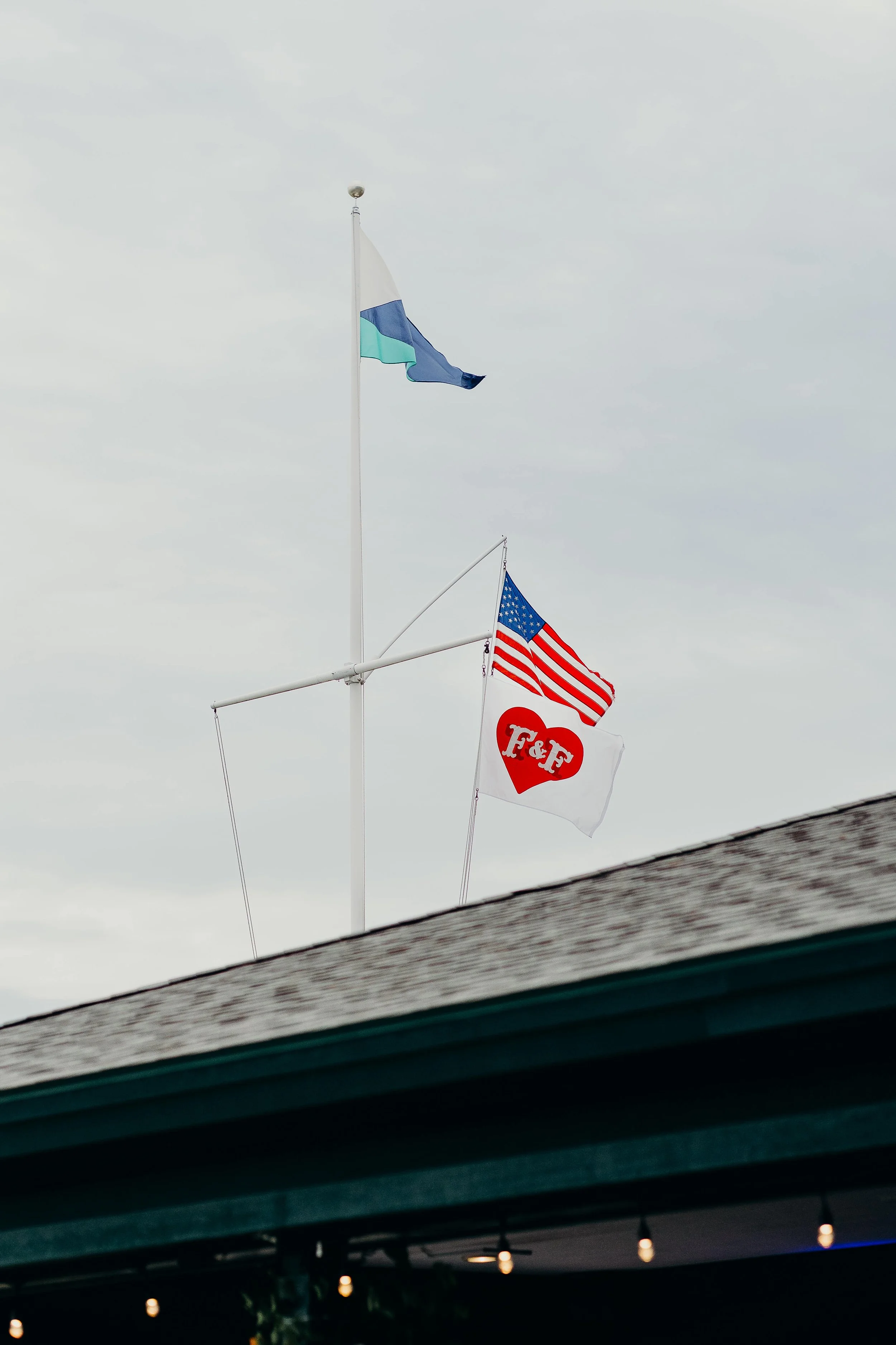 Custom couples monogram flag and American flag flying above Kollegewidgwok Yacht Club in Blue Hill, Maine, wedding venue detail by Milkweed Floral Co
