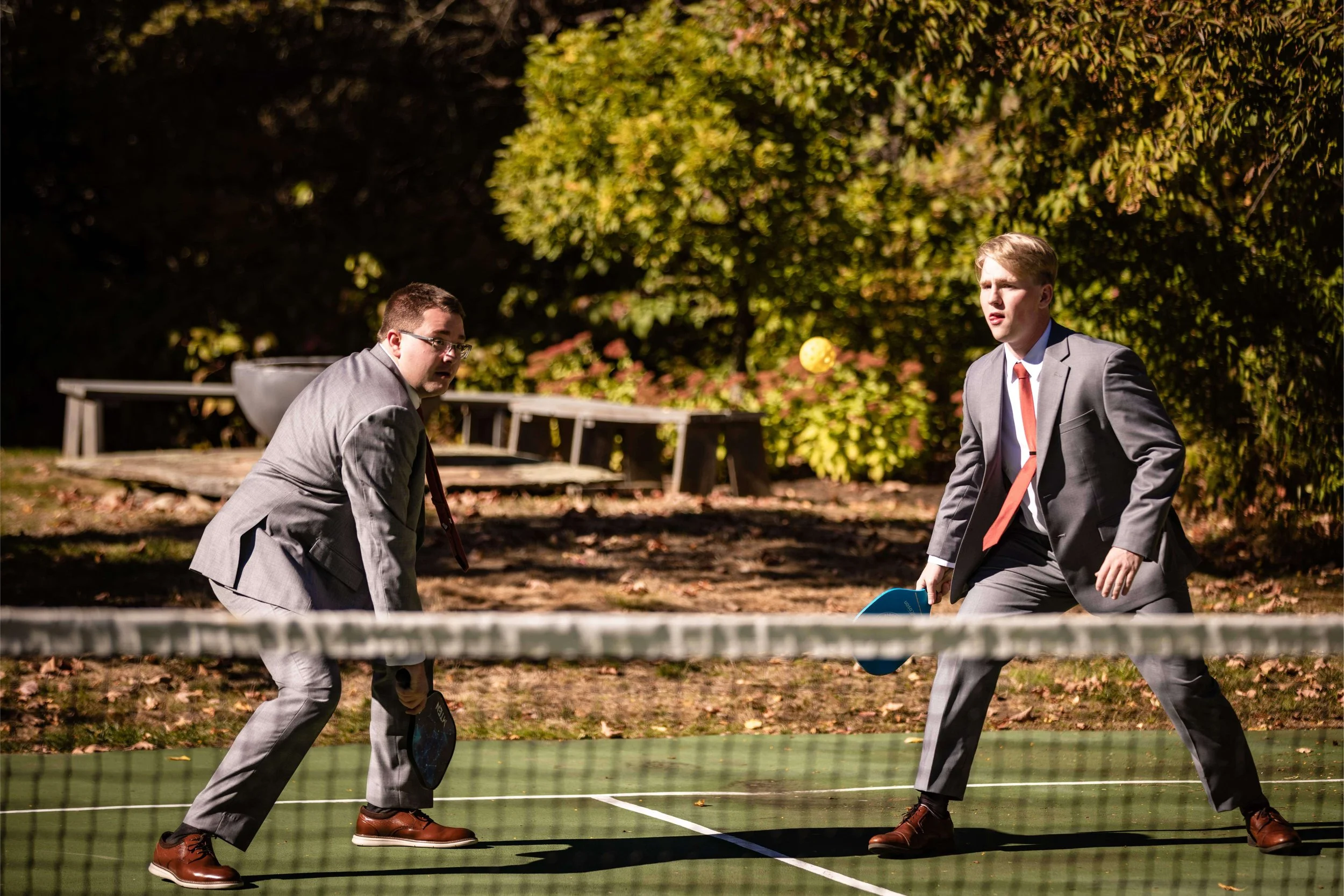 Two men dressed in gray suits playing pickleball, The Barn at Walnut Hill in North Yarmouth, Maine, wedding florals by Milkweed Floral Co