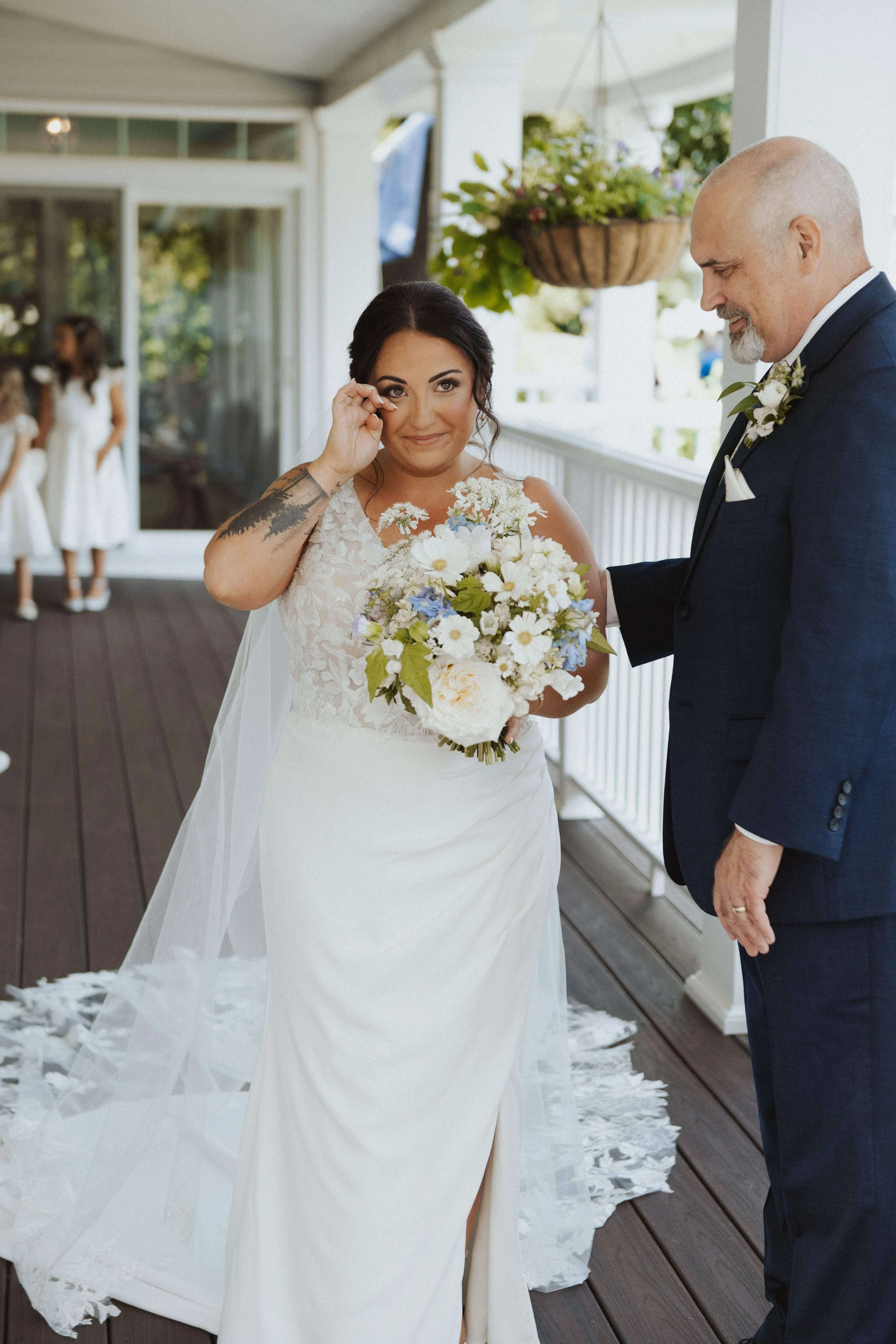 Bride holding coastal inspired bouquet, wiping tear from her face on outdoor porch with father, wedding florals by Milkweed Floral Co