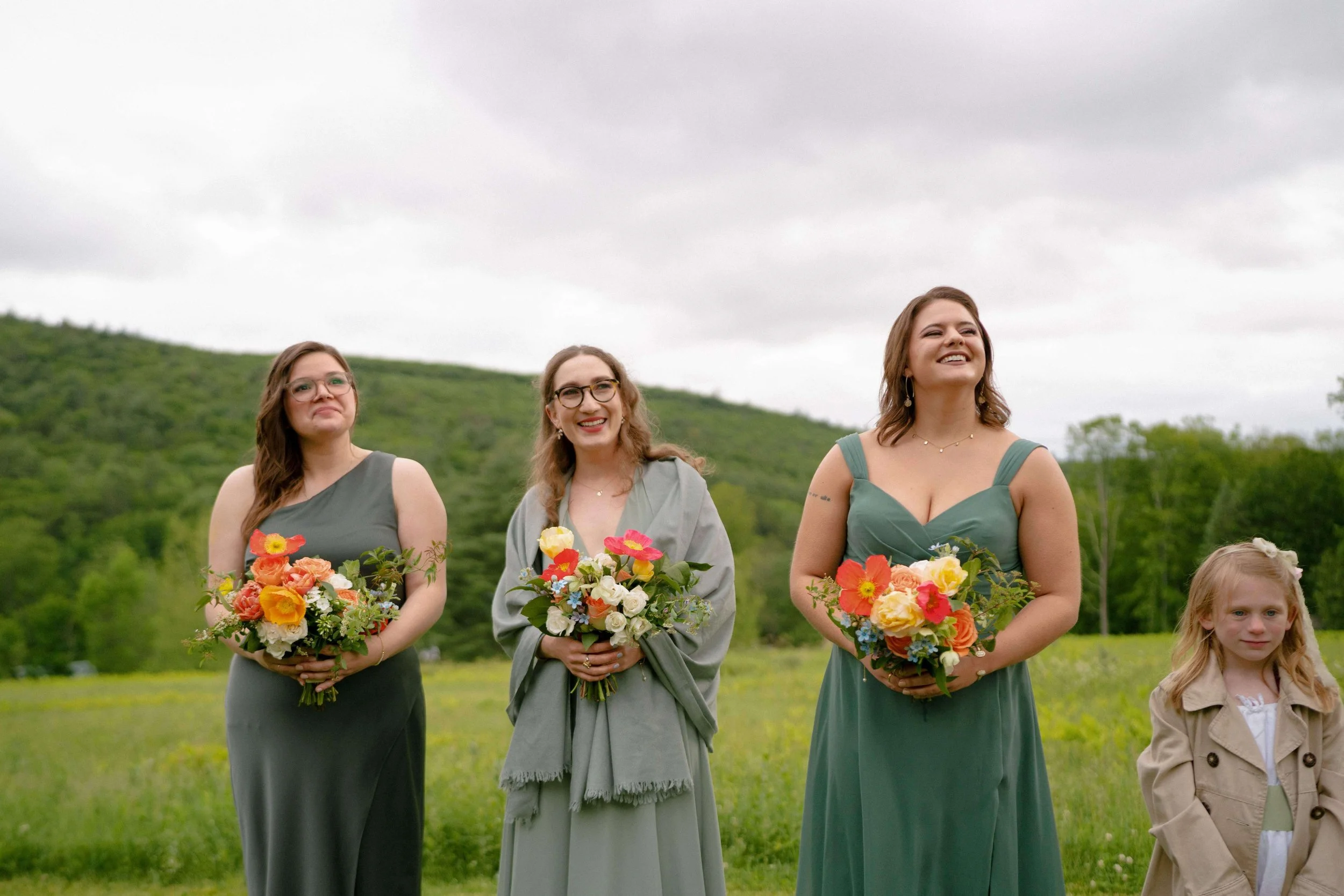 Bridesmaids in sage green with vibrant spring bouquets of orange poppies and yellow ranunculus, New England mountain meadow, Milkweed Floral Co