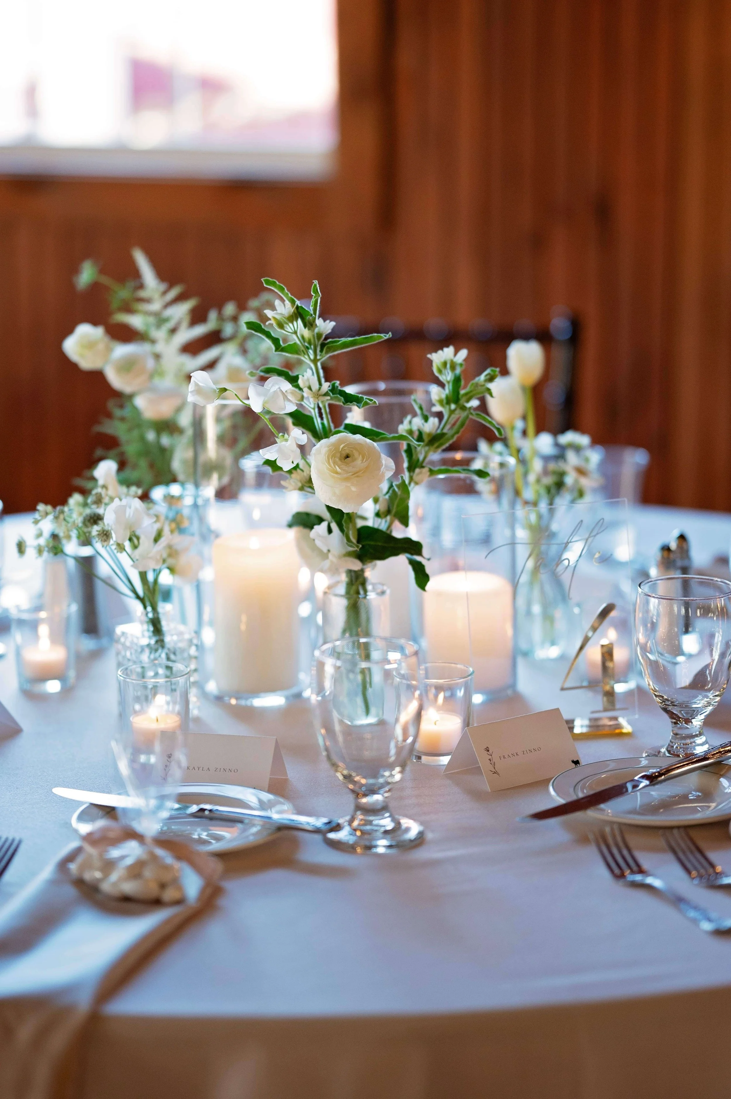Elegant reception table with white ranunculus, tulips, and sweet pea bud vases, pillar candles, and votives at Newfound Lake Inn, Bridgewater New Hampshire wedding florals by Milkweed Floral Co