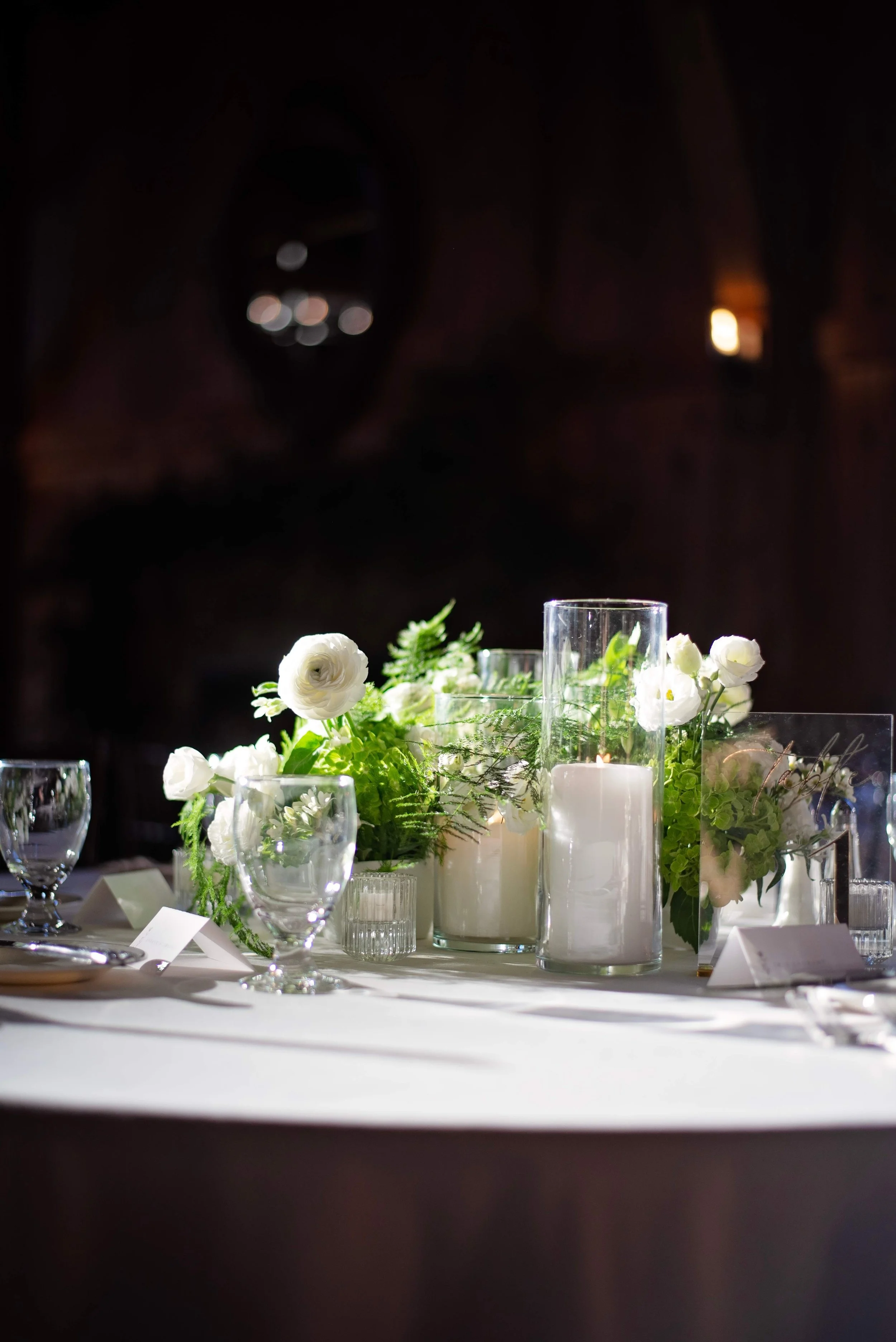 White ranunculus and lush fern low centerpiece with pillar candles and votives at Newfound Lake Inn, Bridgewater New Hampshire wedding florals by Milkweed Floral Co