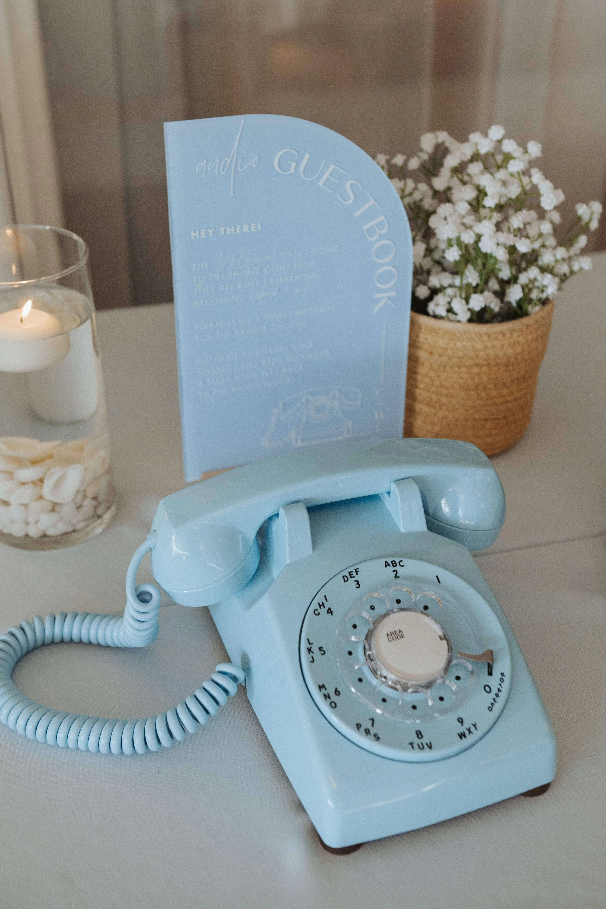 Baby blue rotary phone with sign instructing guests to use it as the guest book, small basket of baby's breath beside sign, Milkweed Floral Co