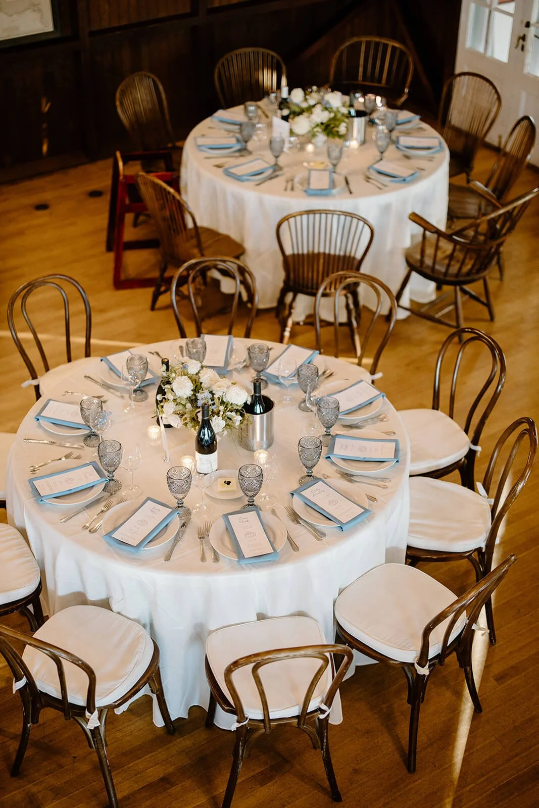 Coastal wedding reception tables with white linens, blue napkins, smoky glassware, and white and blue floral centerpieces at Camden Yacht Club, Maine, Milkweed Floral Co
