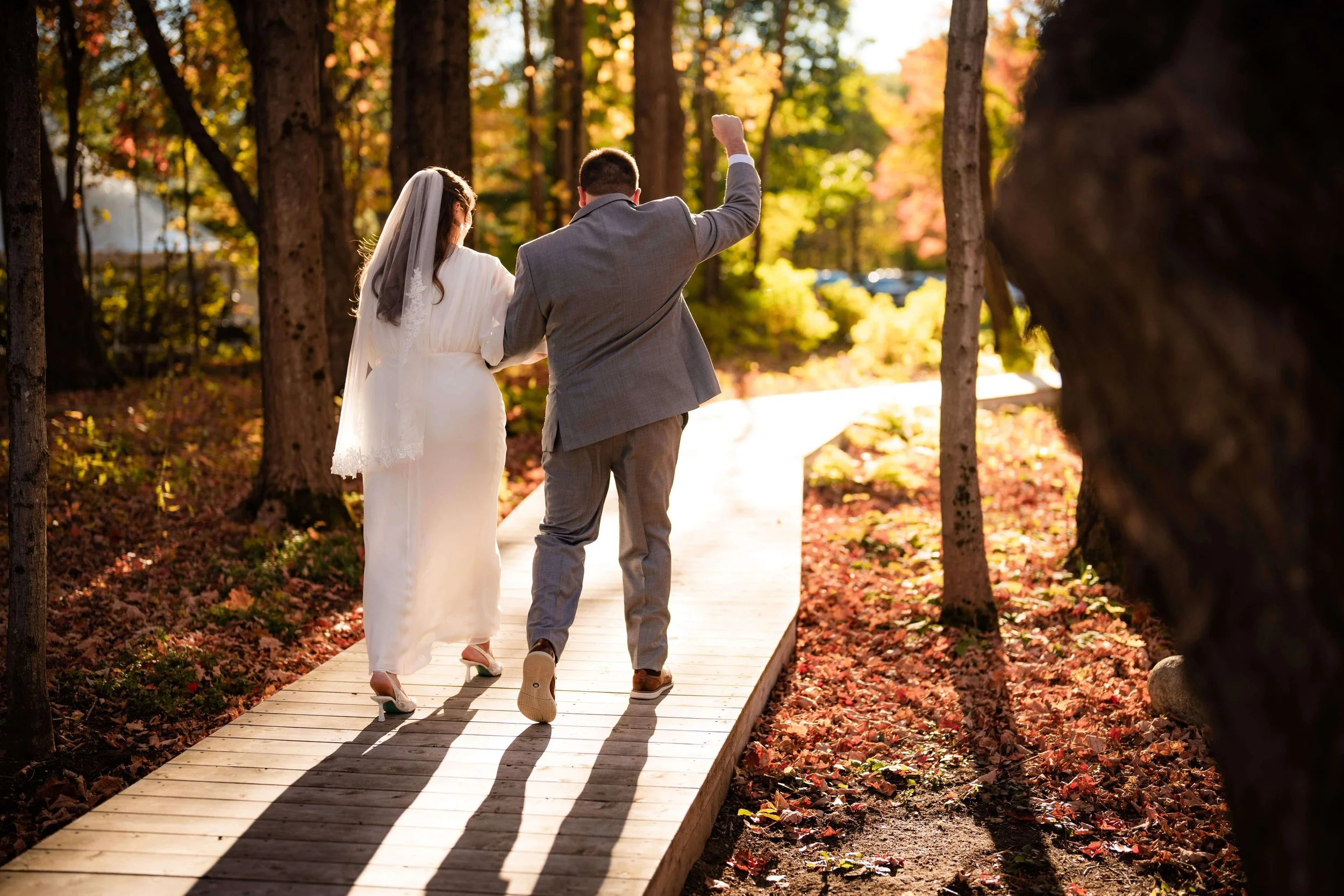 Bride and groom walking toward the sun on garden path, groom has fist in the air in joy,fall wedding, Maine, florals by Milkweed Floral Co