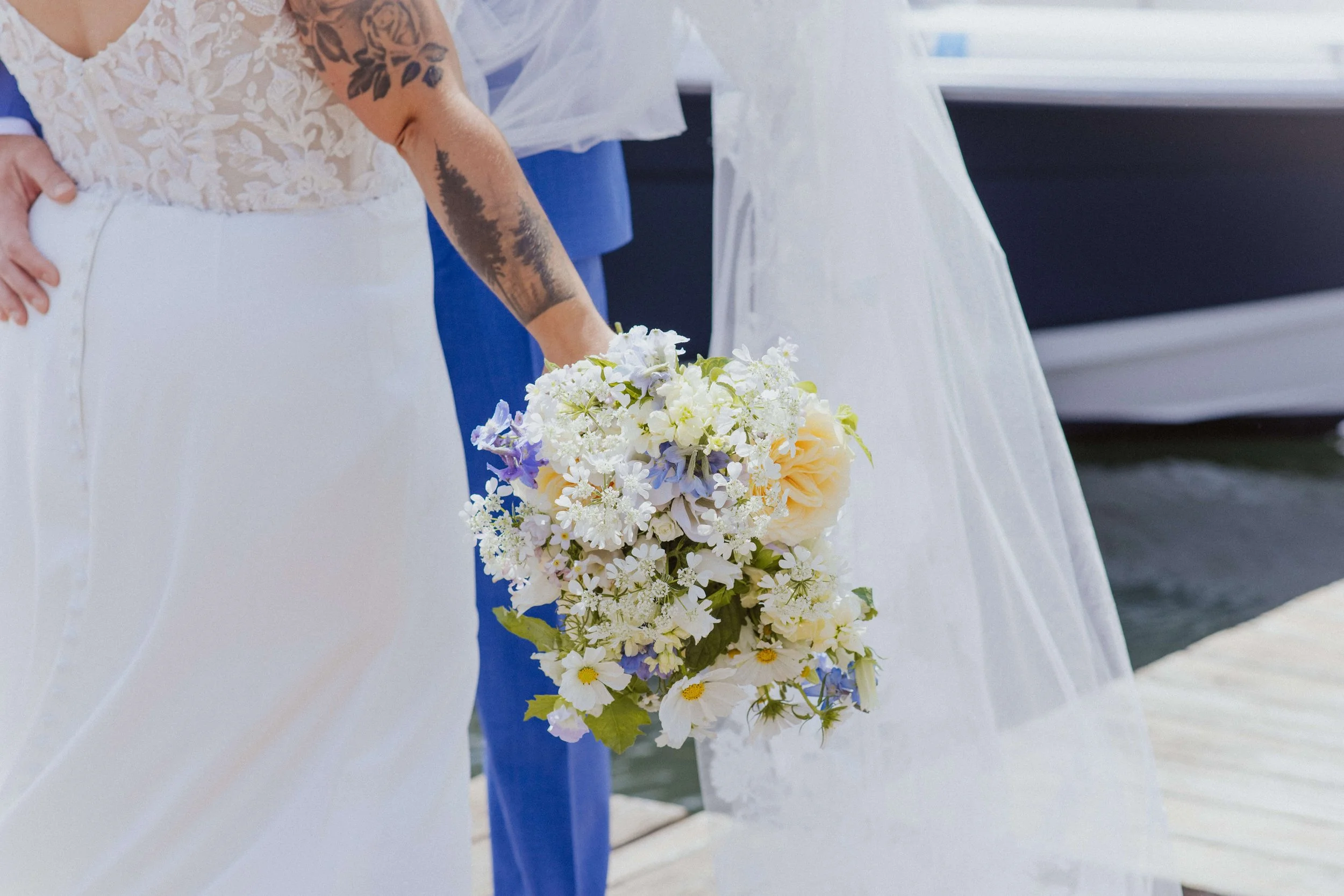Bride holding a loose, garden-style bouquet of white cosmos, lavender delphinium, peach roses, and queen anne's lace on a coastal Maine dock, wedding florals by Milkweed Floral Co