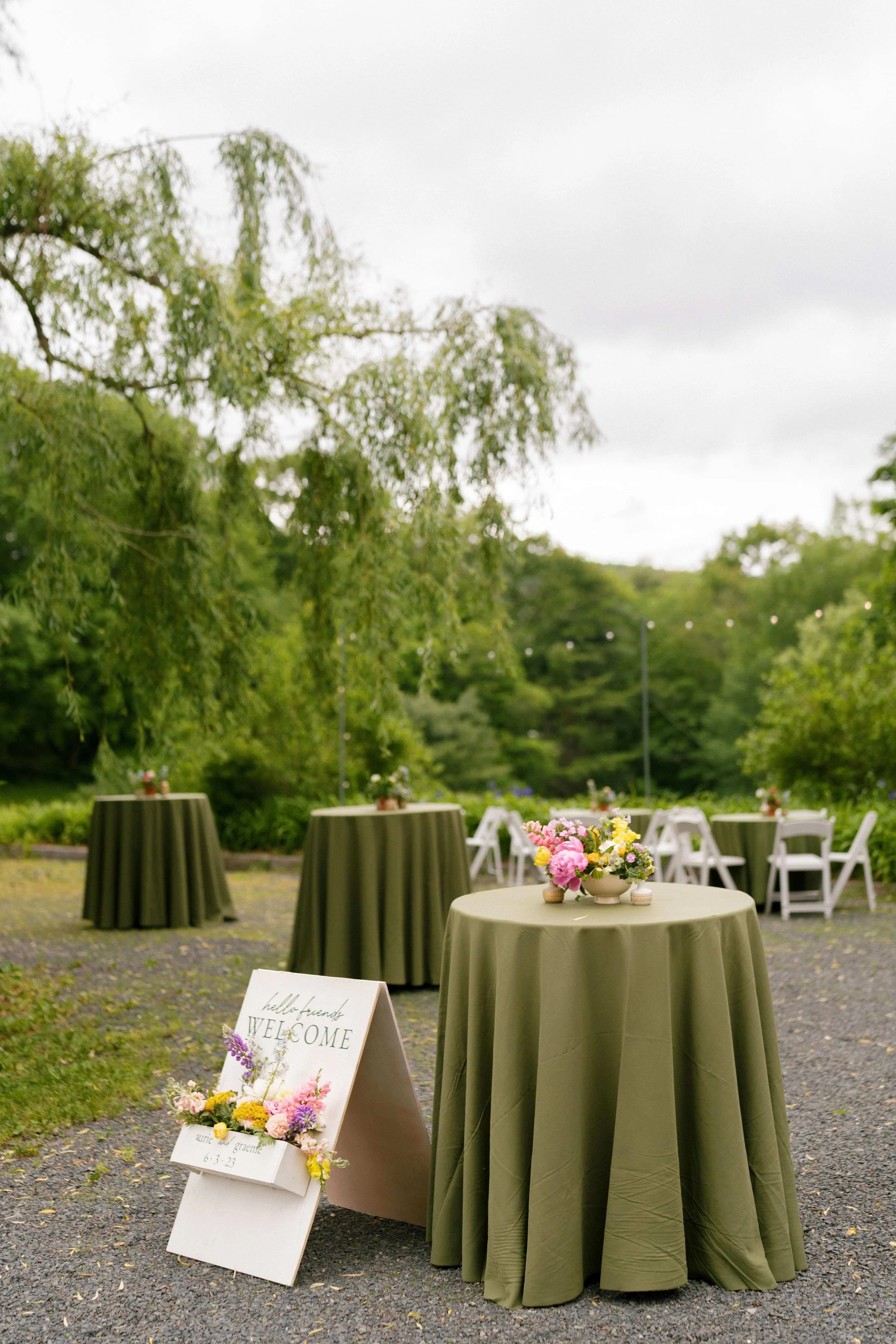 Outdoor cocktail hour with sage green linens and colorful garden floral arrangements and welcome sign, Milkweed Floral Co
