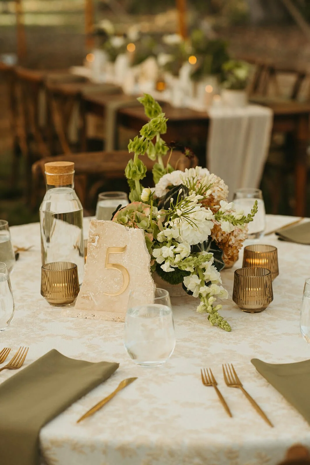 Modern wedding table setting with a white and green centerpiece of hydrangea, dahlias, and hellebores, stone table number, sage green napkins, and gold cutlery, Monson Massachusetts, Milkweed Floral Co