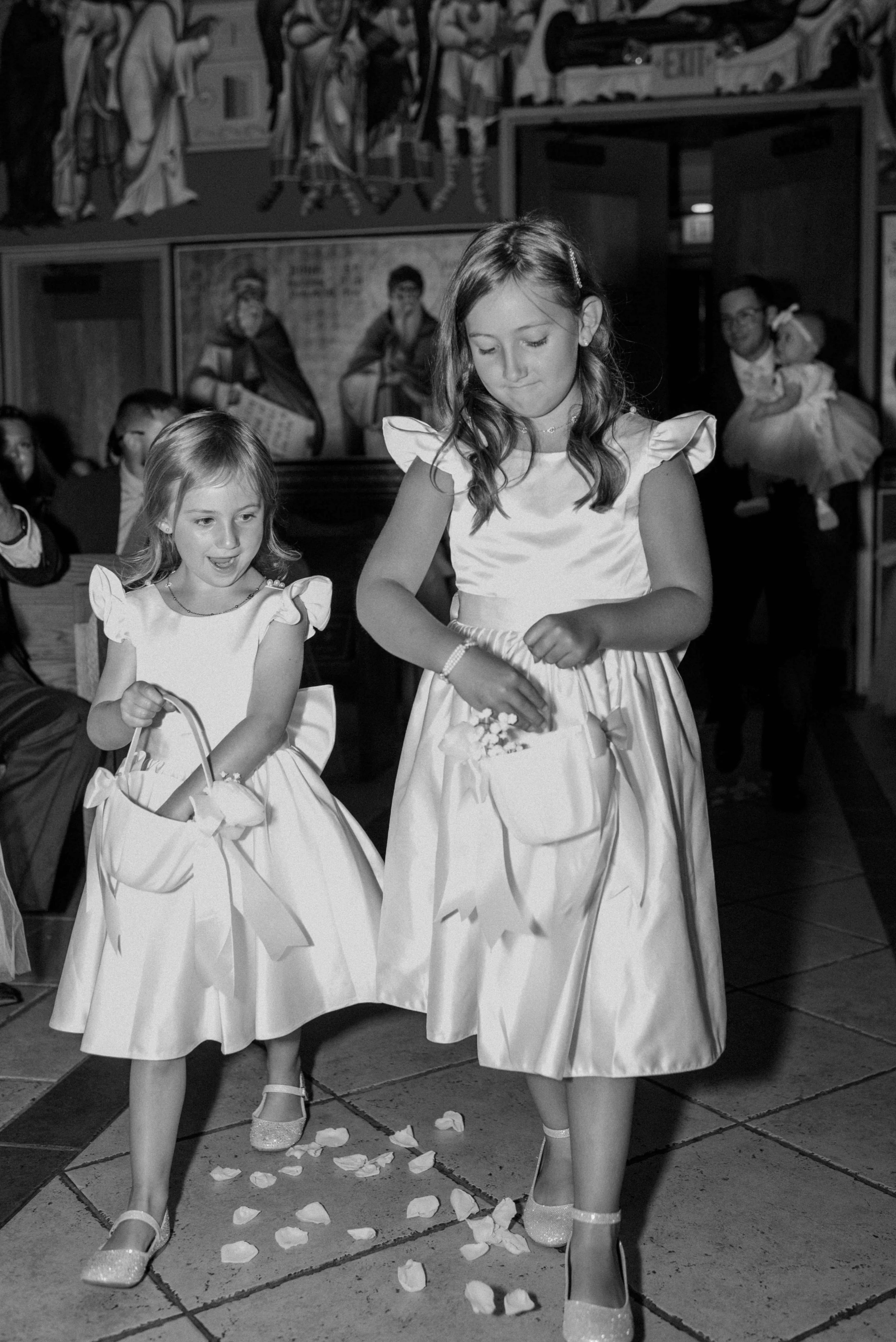 Black and white photograph of flower girls wearing matching dresses and throwing petals during processional, Milkweed Floral Co