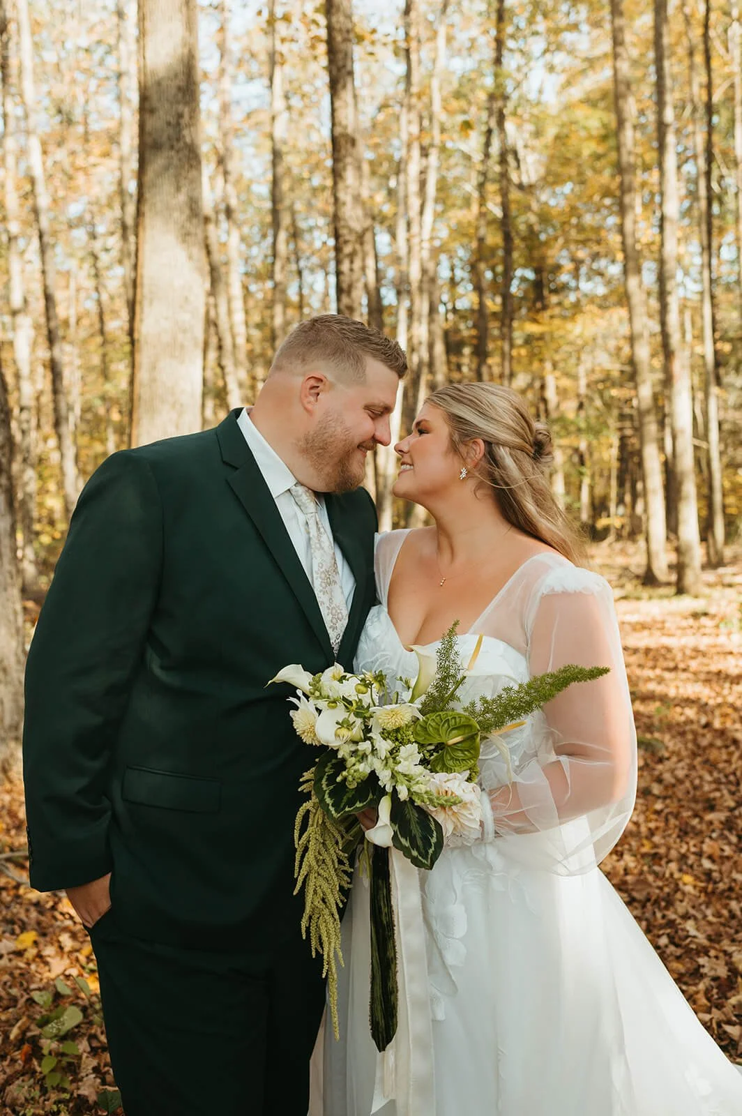 Bride and groom touching foreheads in a fall forest, bride holding a bouquet of white calla lilies and anthurium, Monson Massachusetts, Milkweed Floral Co