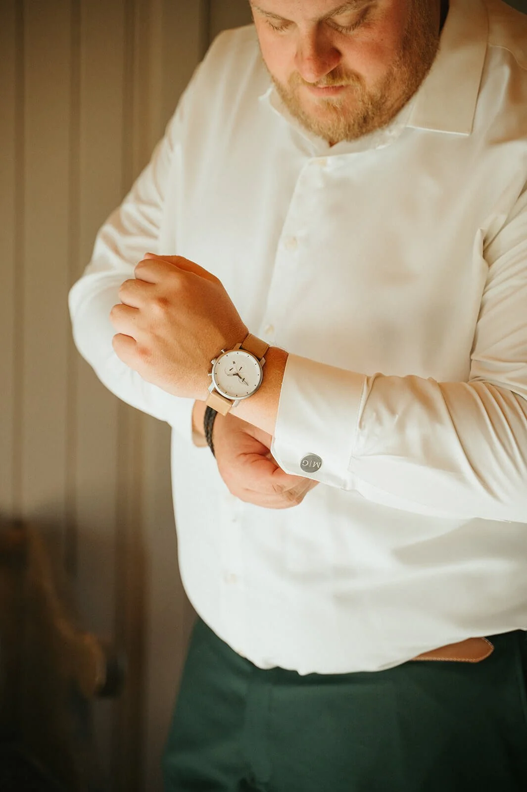 Groom in a white dress shirt with monogram cufflinks fastening a tan leather watch, getting ready detail for a Monson Massachusetts wedding by Milkweed Floral Co