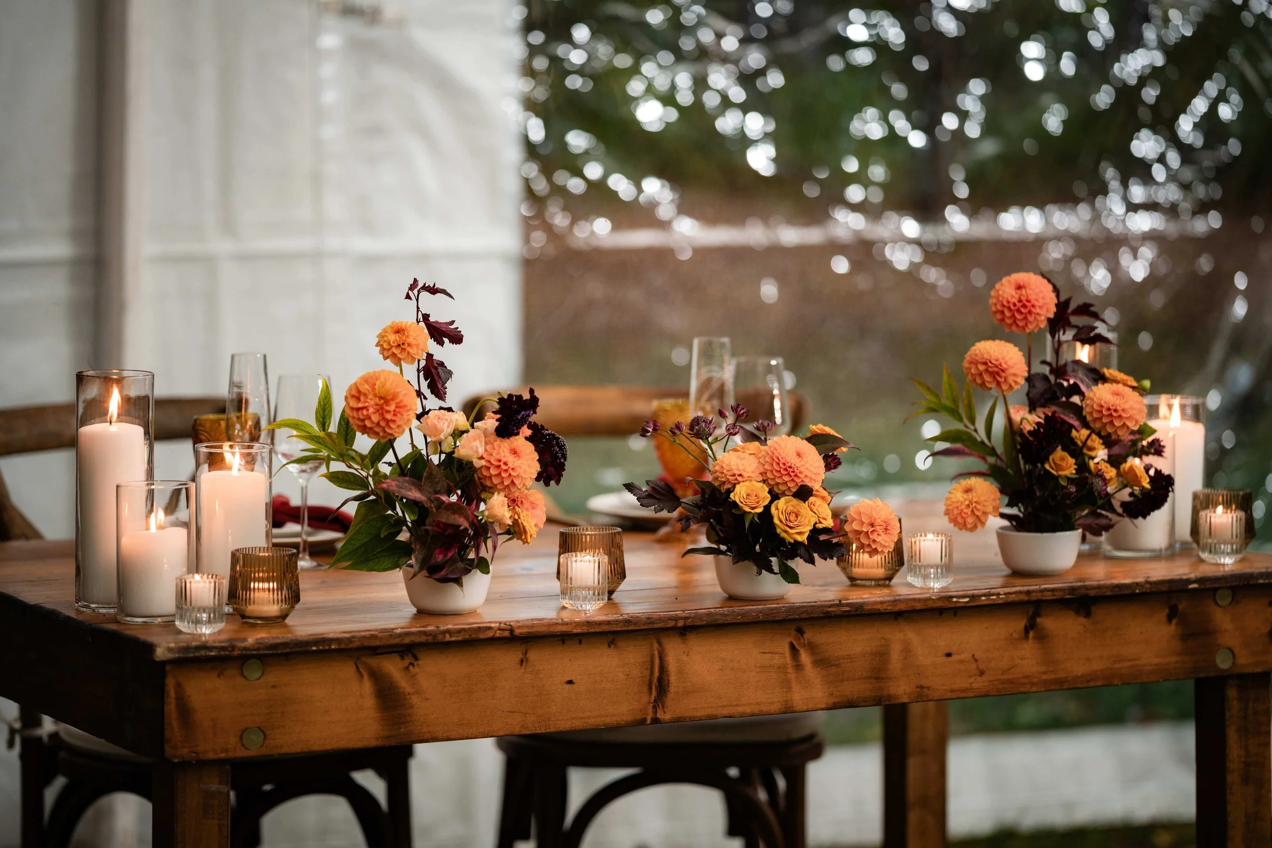 Rustic sweetheart table with peach and orange dahlia arrangements, dark burgundy foliage, and yellow roses in white vessels surrounded by candlelight, Barn on Walnut Hill wedding by Milkweed Floral Co