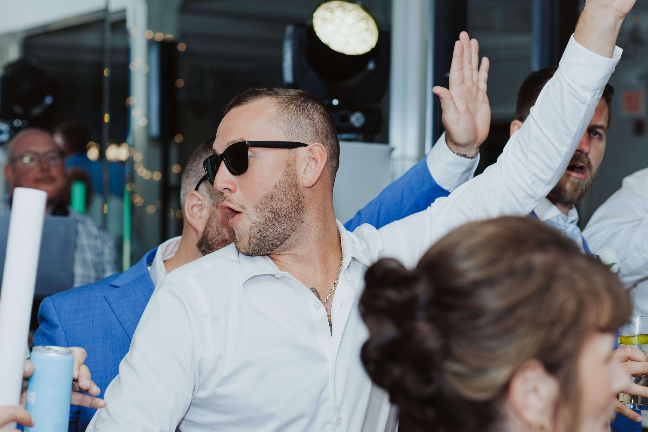 Wedding guest dancing with arm raised in the air, wearing black sunglasses, coastal Maine wedding