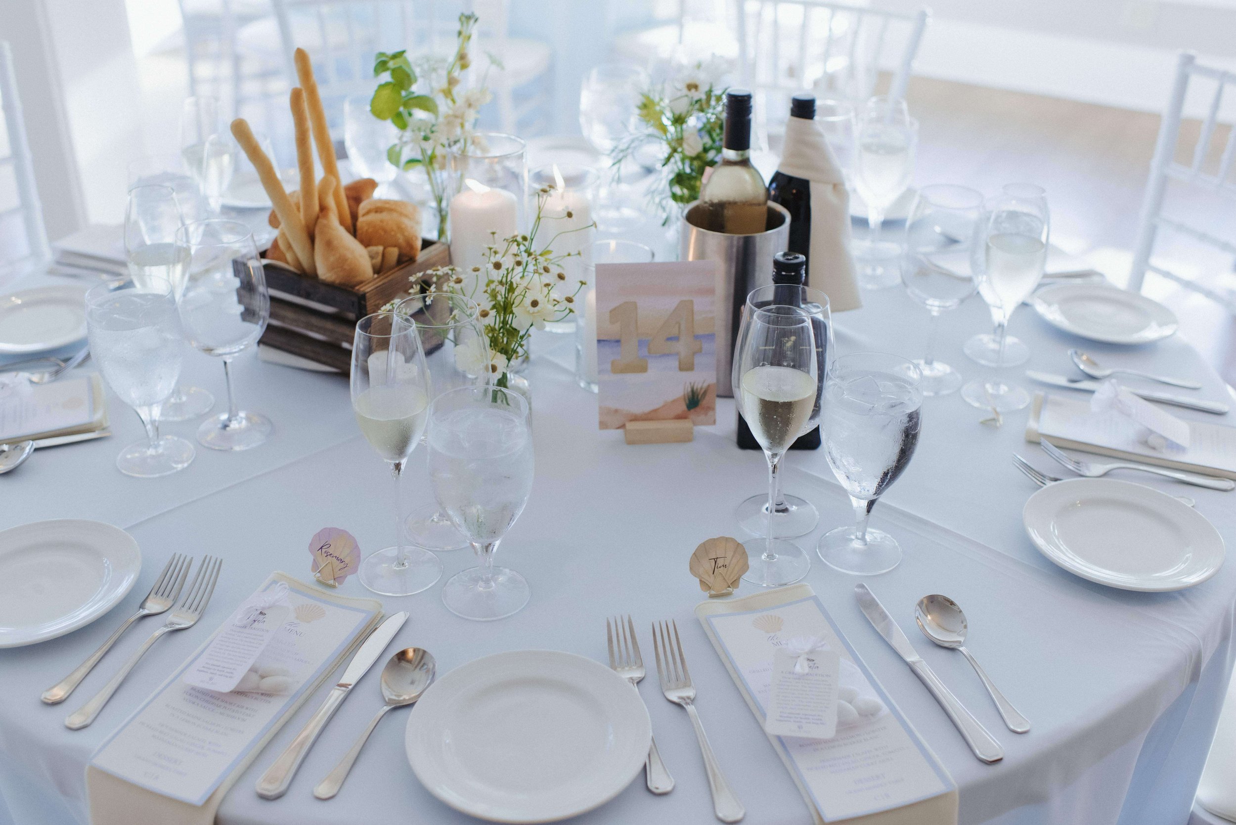 Elegant white table setting with breadsticks and wine bottles, delicate white flowers in clear vases by Milkweed Floral Co, coastal wedding, Maine