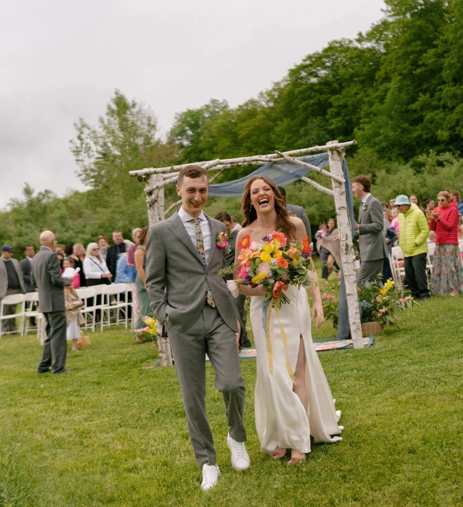 Joyful bride and groom recessional at an outdoor spring wedding with birch arch and vibrant wildflower bouquet, Milkweed Floral Co