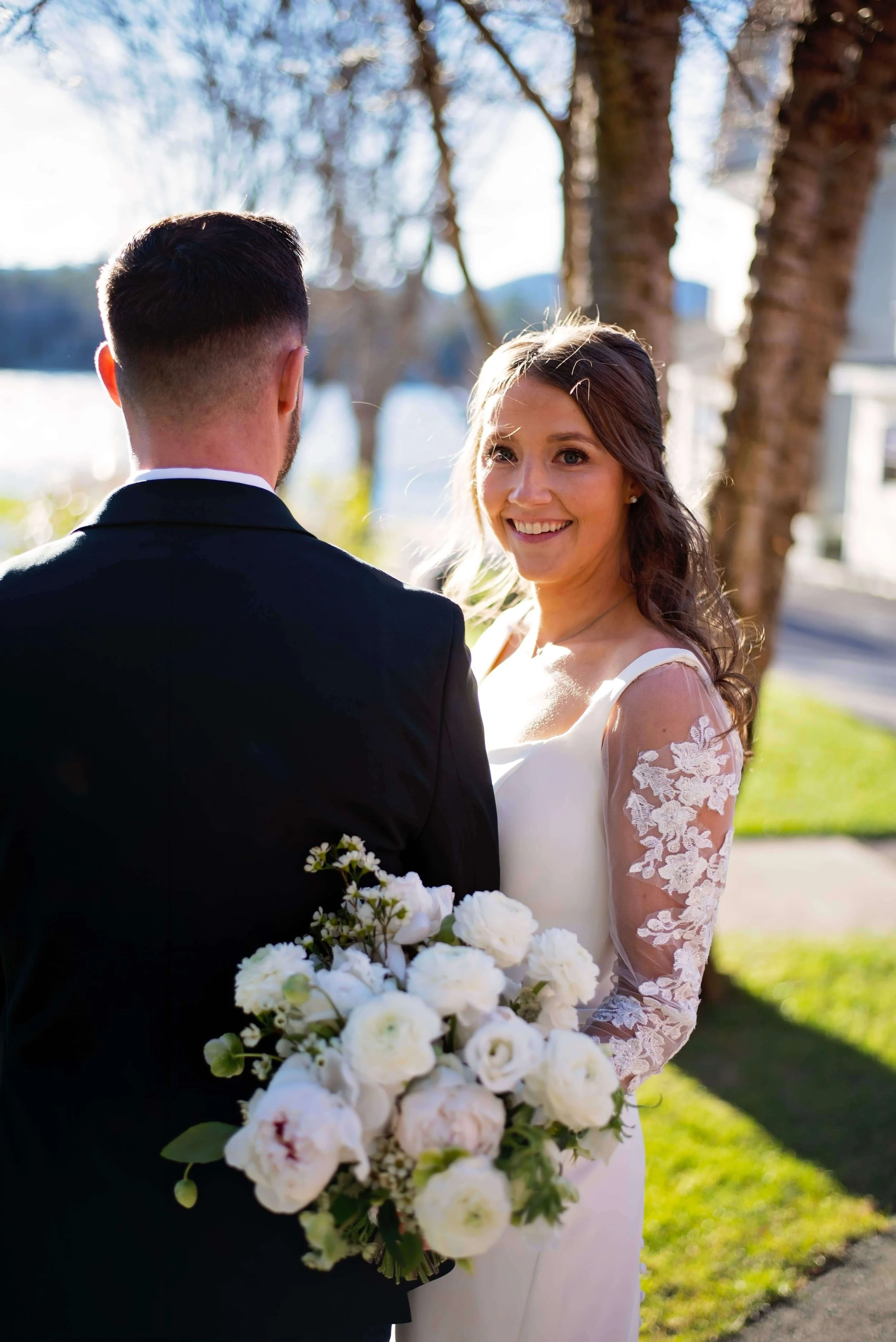 Smiling bride holding a lush white peony and ranunculus bouquet with her groom at Newfound Lake Inn, Bridgewater New Hampshire wedding by Milkweed Floral Co