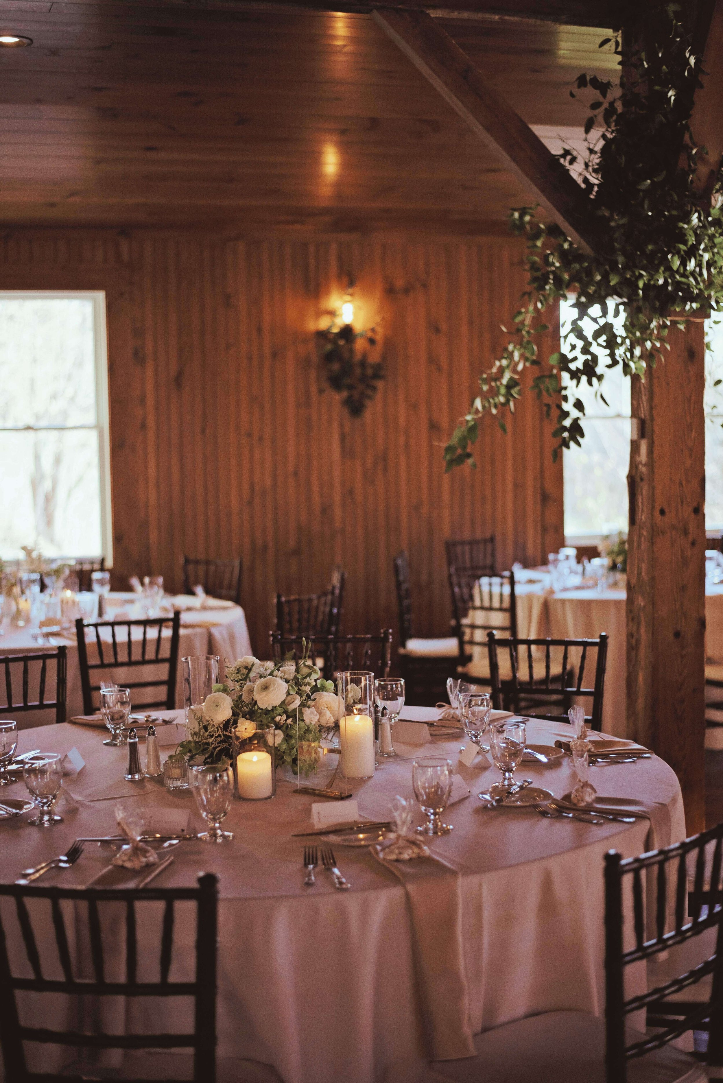 Reception room with white ranunculus centerpieces, pillar candles, and greenery-wrapped beam at Newfound Lake Inn, Bridgewater New Hampshire wedding florals by Milkweed Floral Co