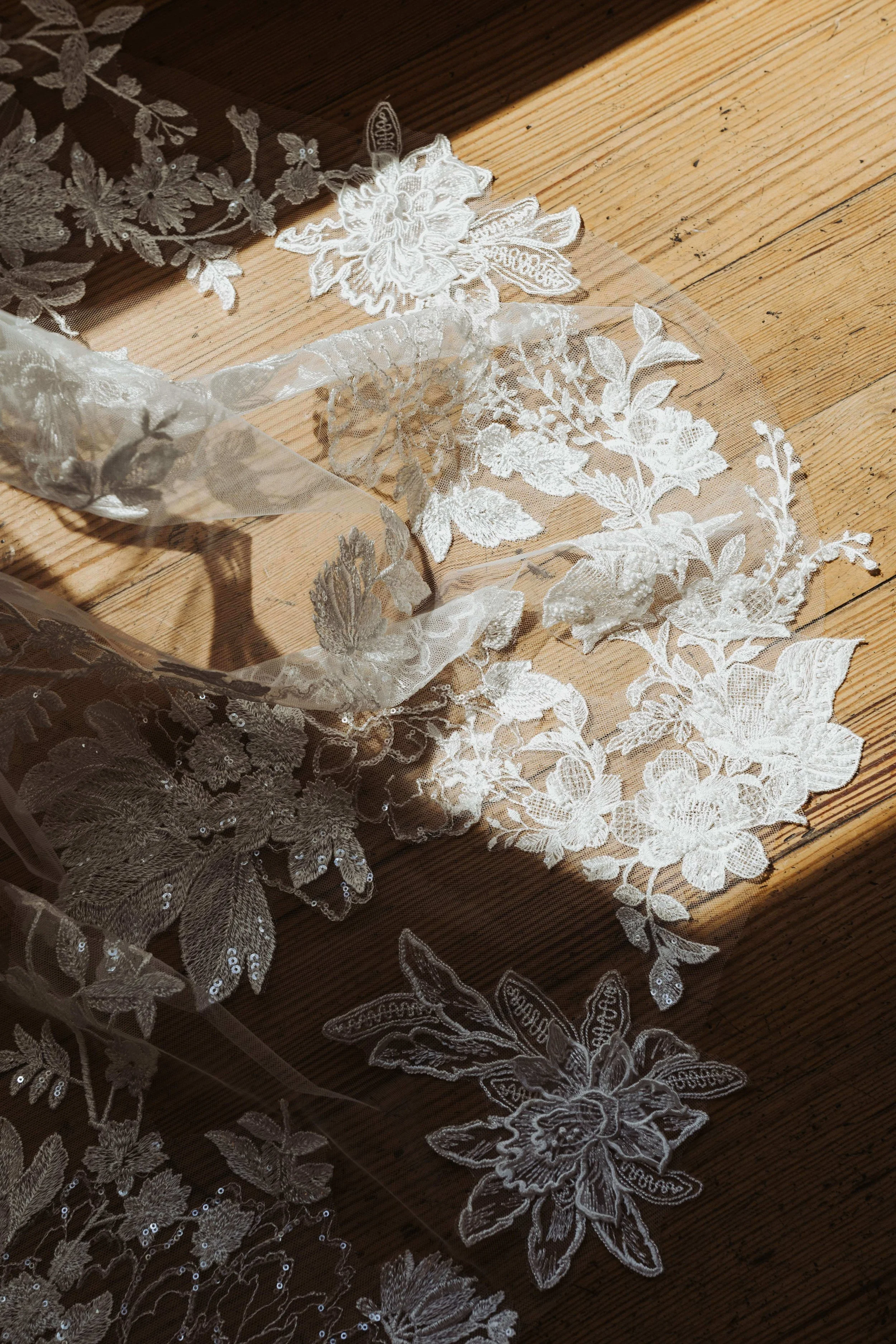 Delicate floral lace appliqués and embroidered tulle spread across a sunlit wood floor, Maine wedding, Nonantum Resort