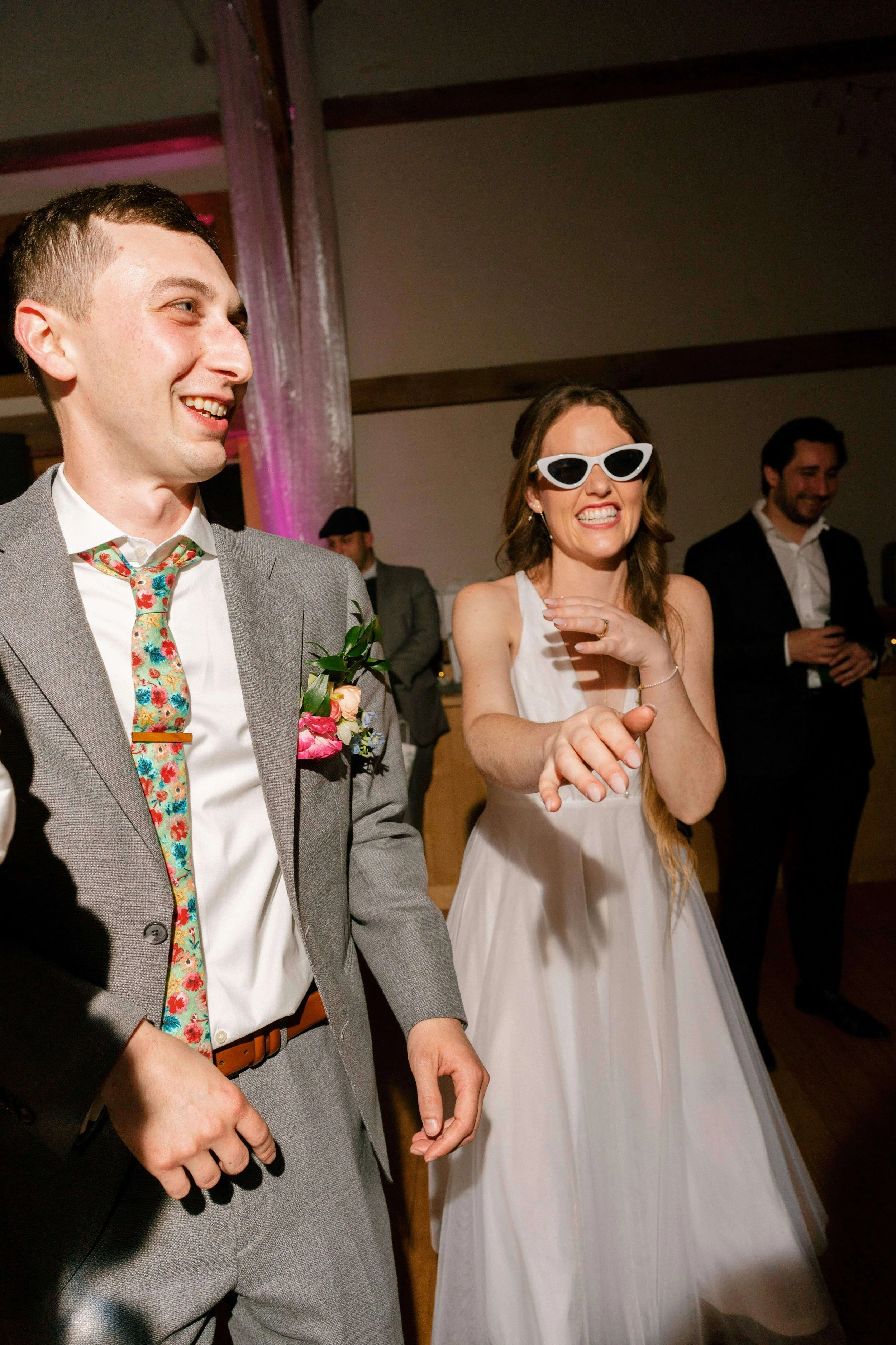Bride wearing white cat-eye sunglasses dancing with the groom at a wedding reception, groom wearing a colorful floral boutonniere and floral tie, Montague Retreat Massachusetts, Milkweed Floral Co