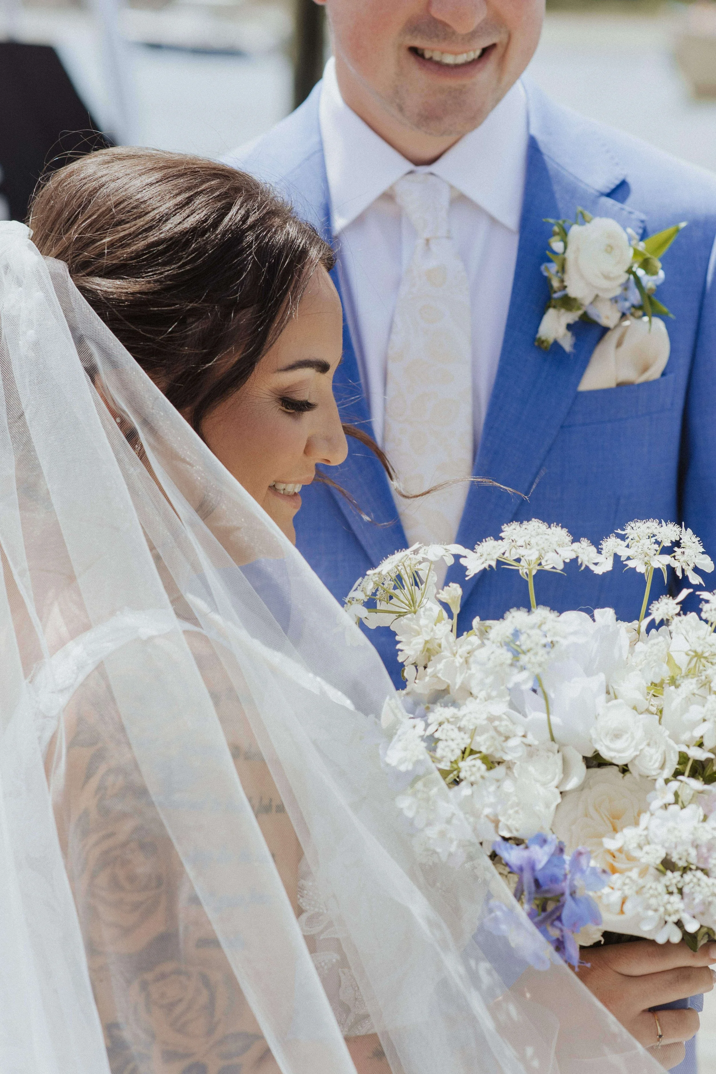 Happy bride and groom smiling outside, holding white bridal bouquet, groom dressed in blue linen suit with white boutonneire and white pocket square, Kennebunkport, Milkweed Floral Co