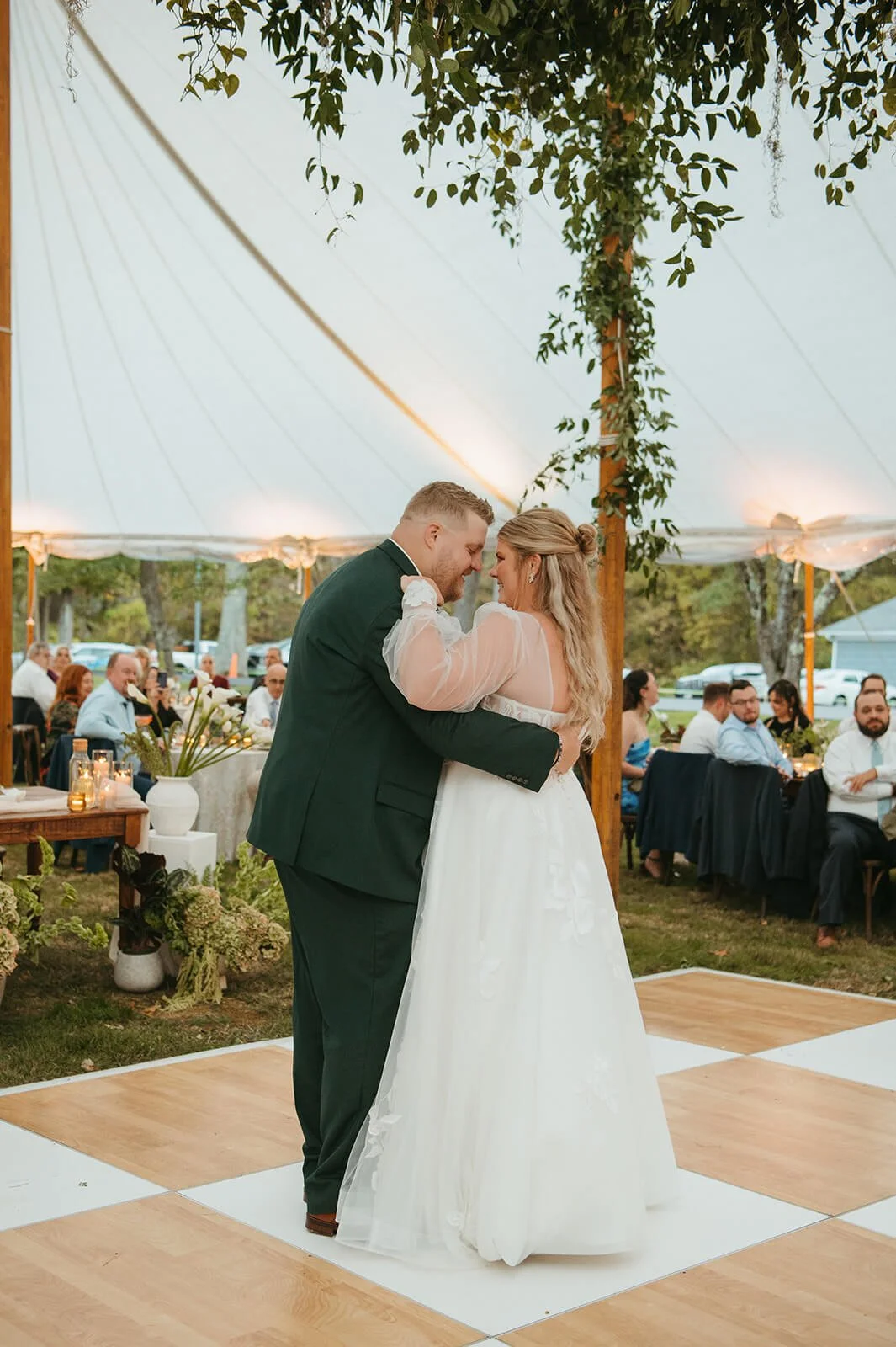 Bride and groom sharing their first dance under a lush hanging greenery installation on a tent pole, with white hydrangea ground arrangements and candlelit tables visible, Monson Massachusetts, Milkweed Floral Co
