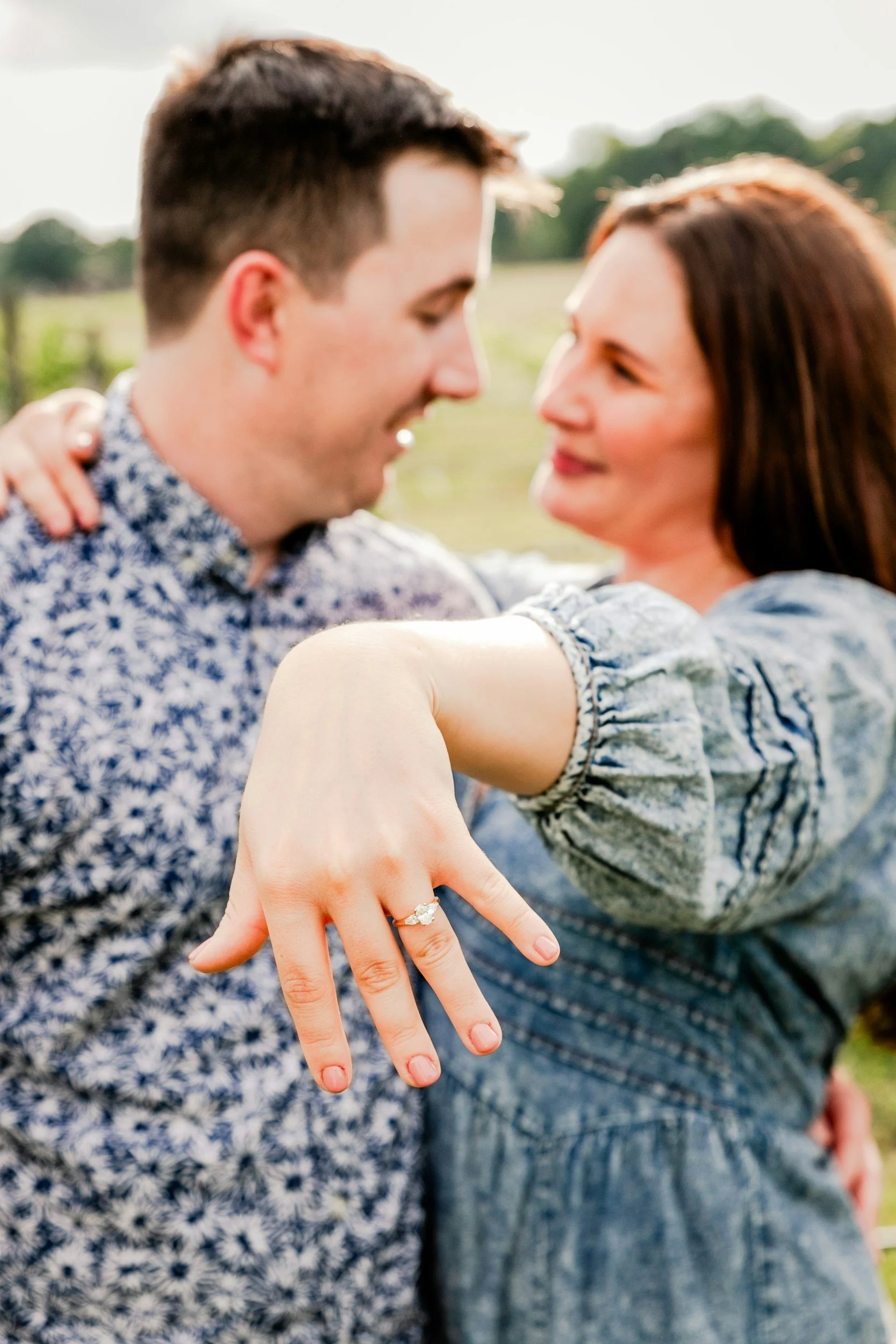 Close-up of a couple showing off their wedding rings with their faces close together outdoors.