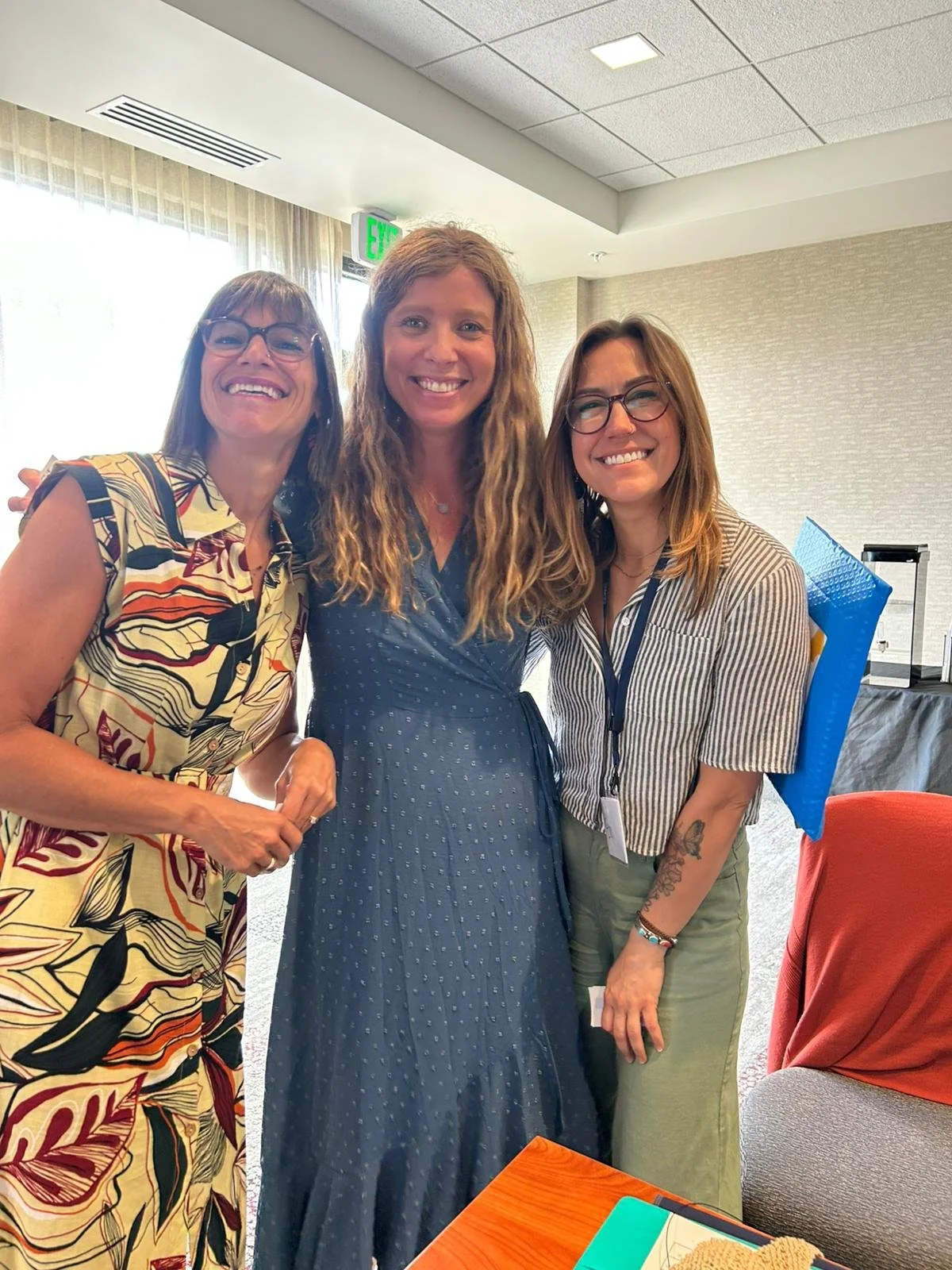 Nina Cashman, executive leadership coach with two women smiling and posing for a photo indoors, with a window with curtains and an exit sign in the background.