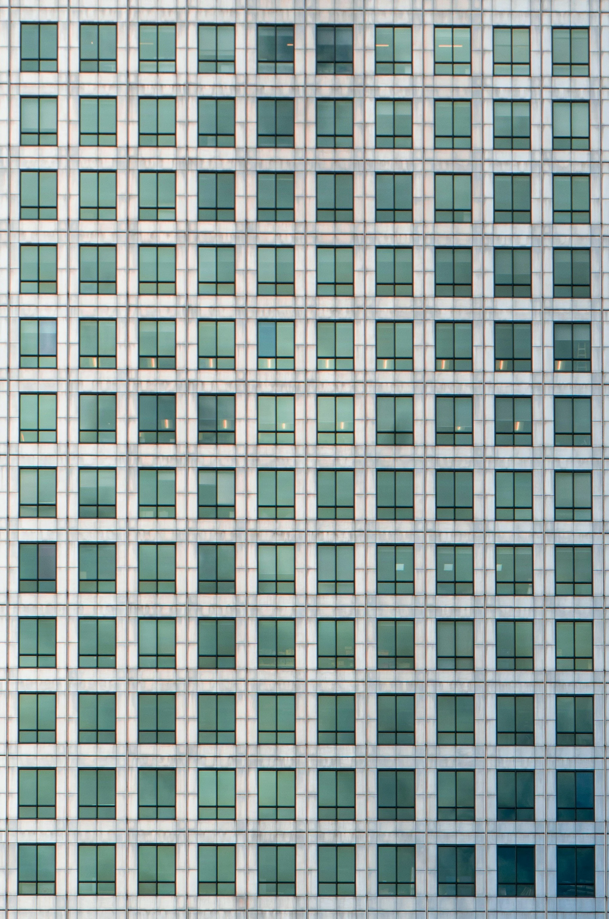 The facade of a tall office building with a grid of uniform green-tinted windows framed by light-colored concrete.