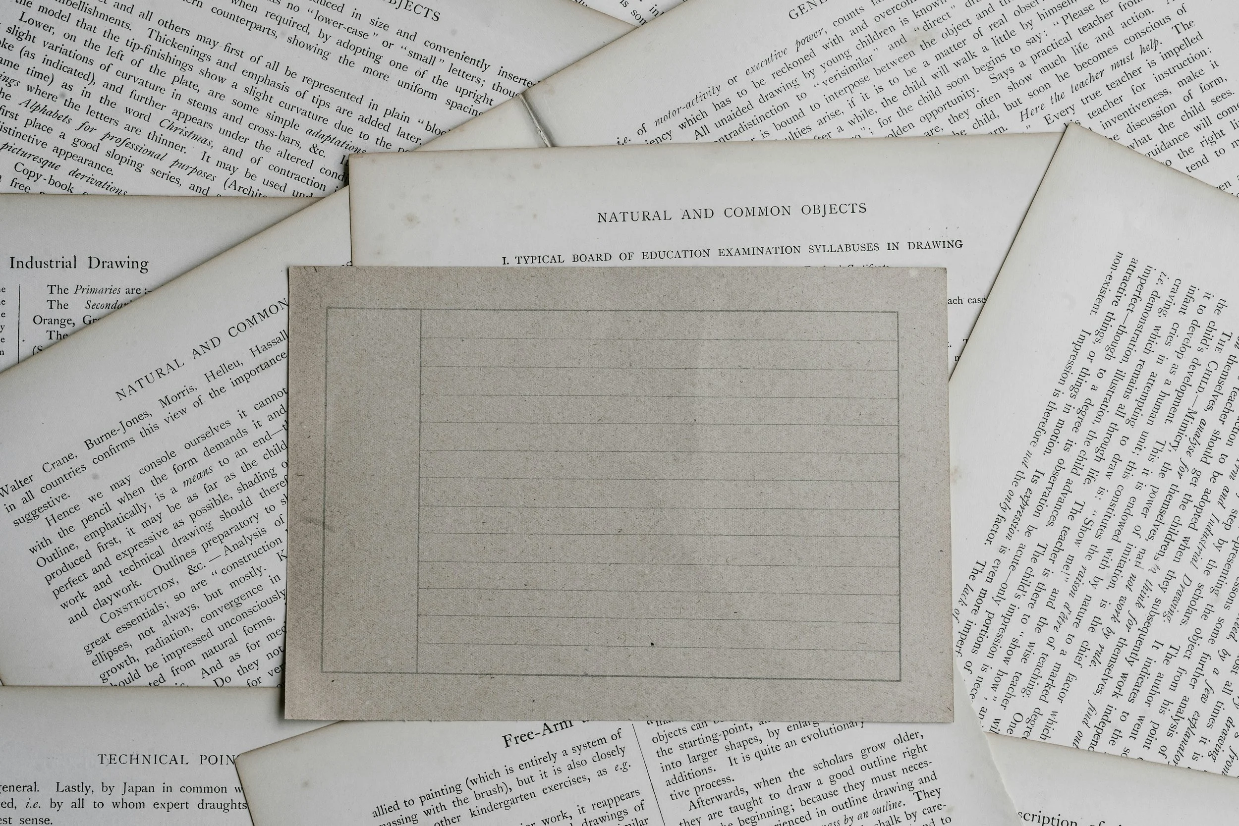 Various old papers and documents scattered, with a gray lined drawing paper in the center titled 'Natural and Common Objects' for a drawing exam.