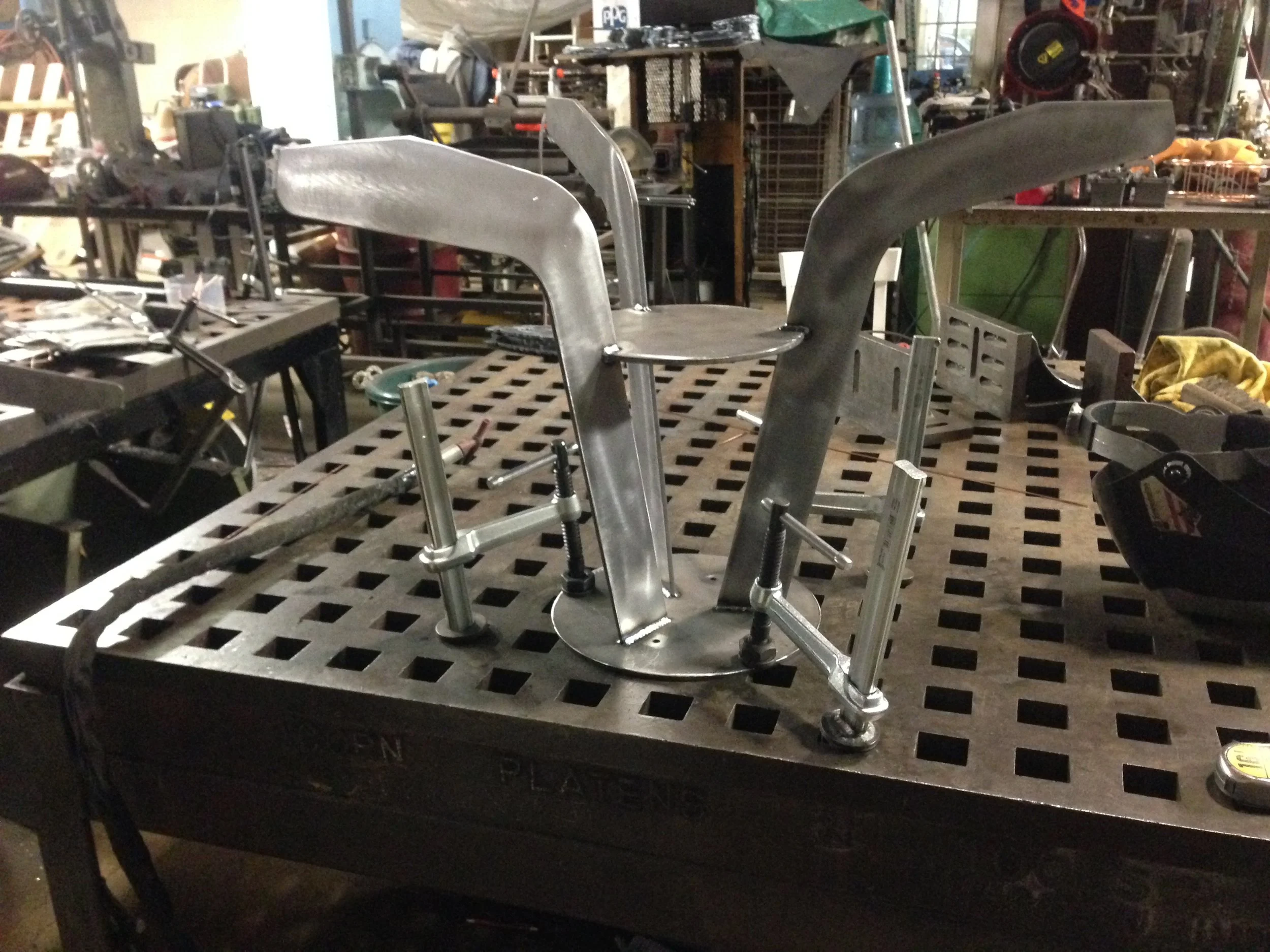 Metalwork fixture on a workbench in a workshop, surrounded by tools and equipment in the background.