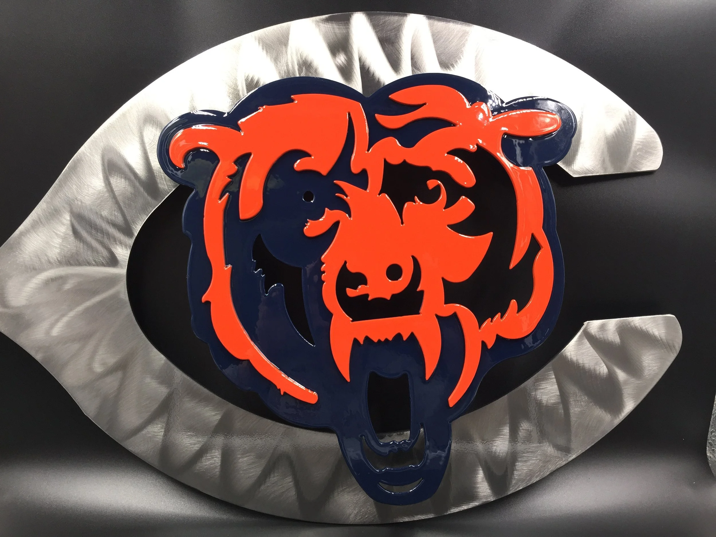 The image features a metallic silver-colored, stylized eye shape with a black background inside. In the center, there is a colorful logo of the Chicago Bears, an NFL football team. The logo has a blue and orange bear's face with a fierce expression, surrounded by a blue outline.
