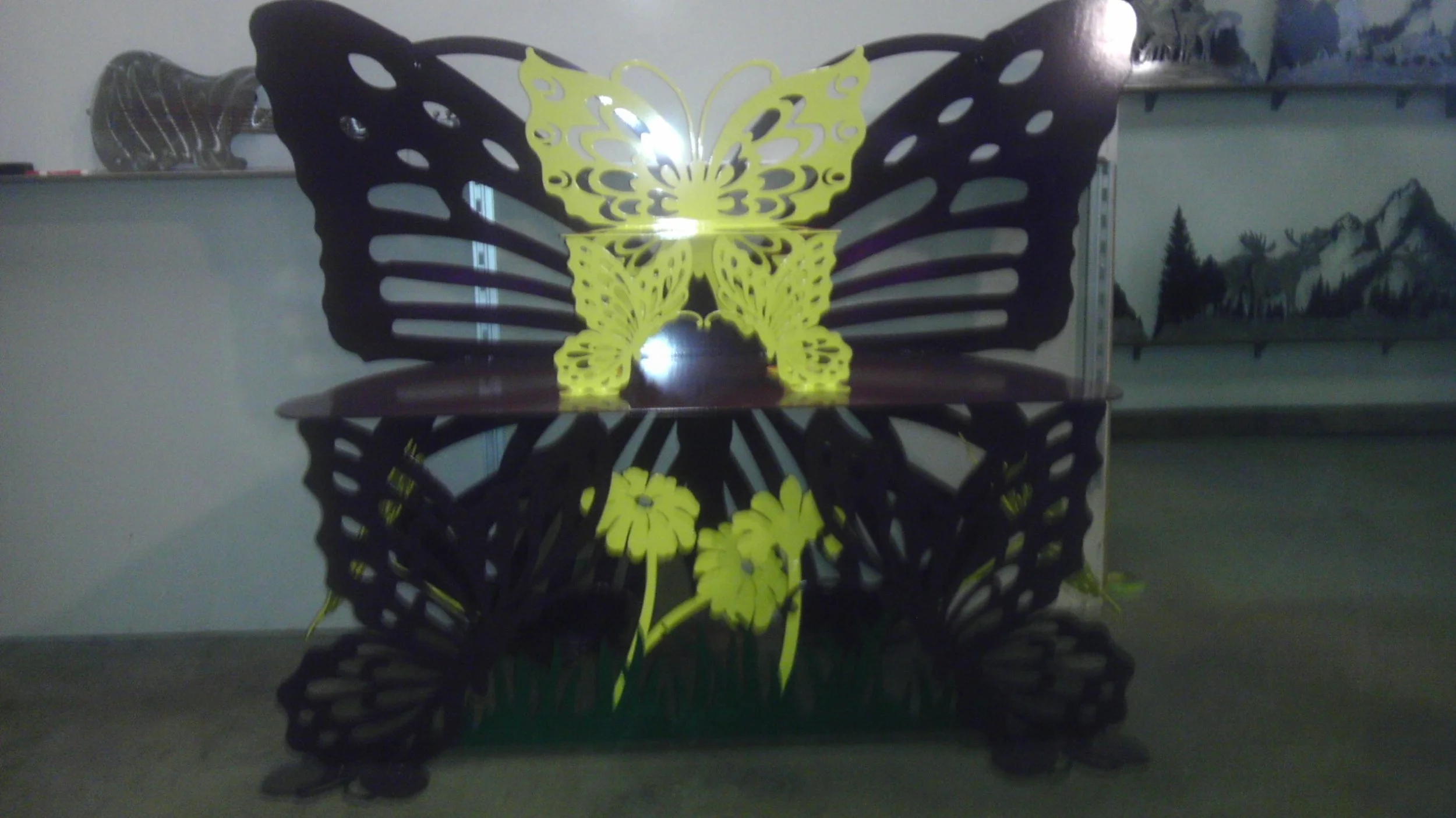 Decorative butterfly-shaped table with yellow and black butterfly design and yellow flowers beneath, in a room with shelves and artwork in the background.