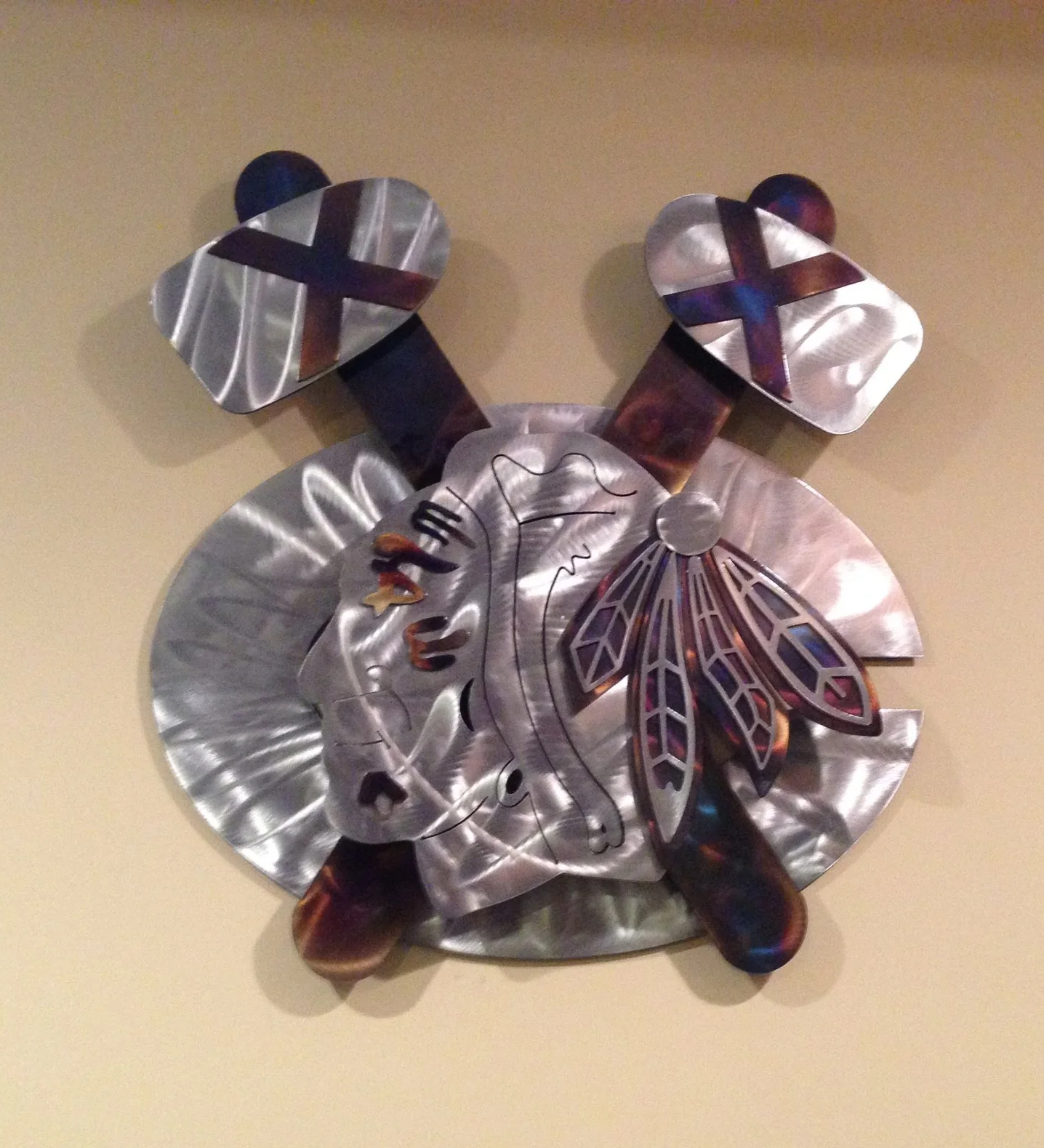 Decorative wall art of a Native American chief in profile, made of metal with feather and face details.