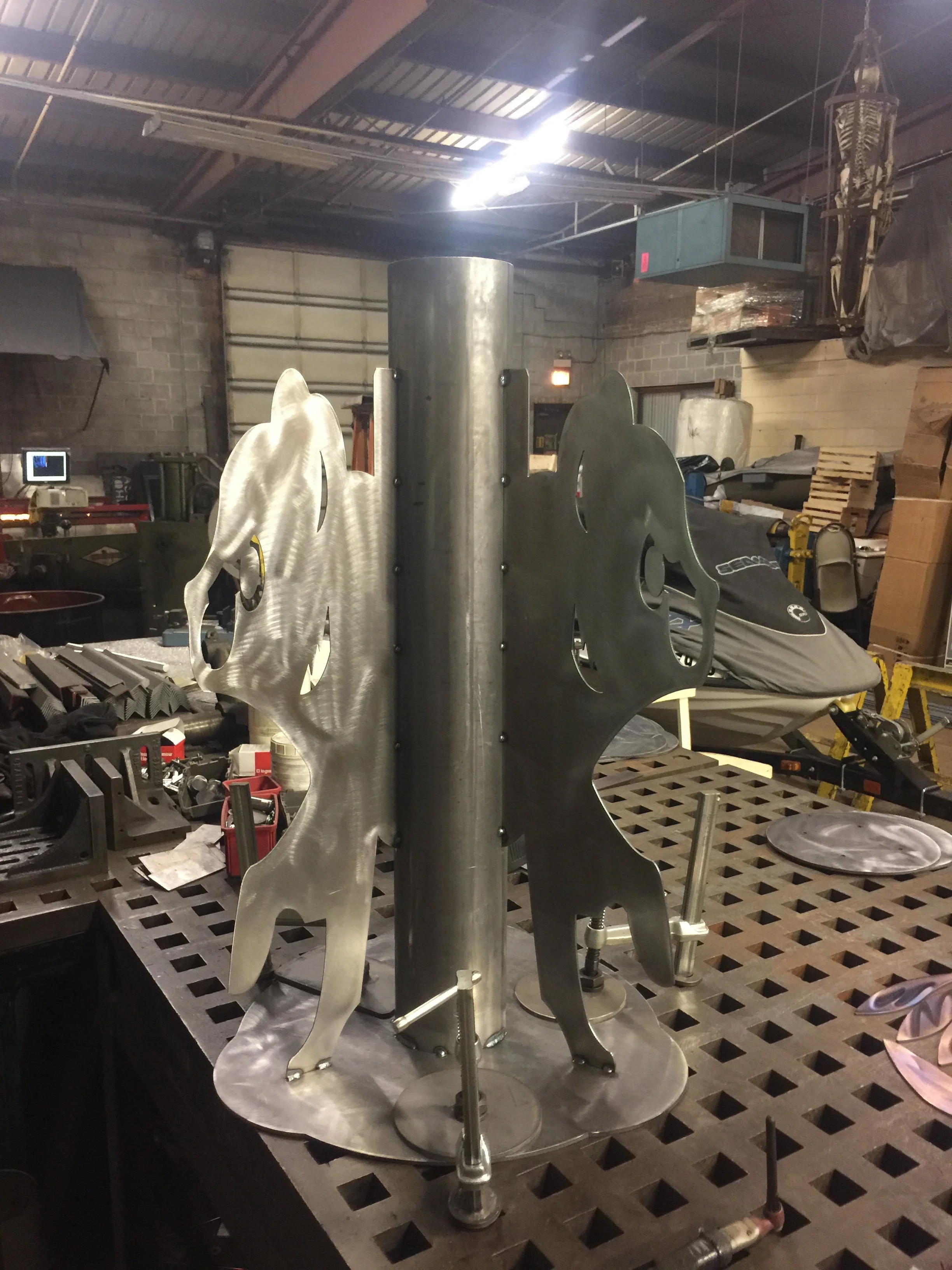 Metal sculpture of four horses with stylized, abstract design, mounted on a workbench in an industrial workshop.
